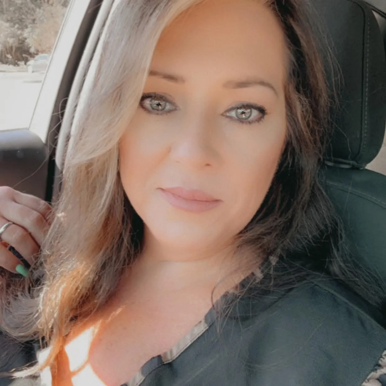 Close-up portrait of a woman with light-colored hair sitting in a vehicle, looking at the camera with a slight smile.