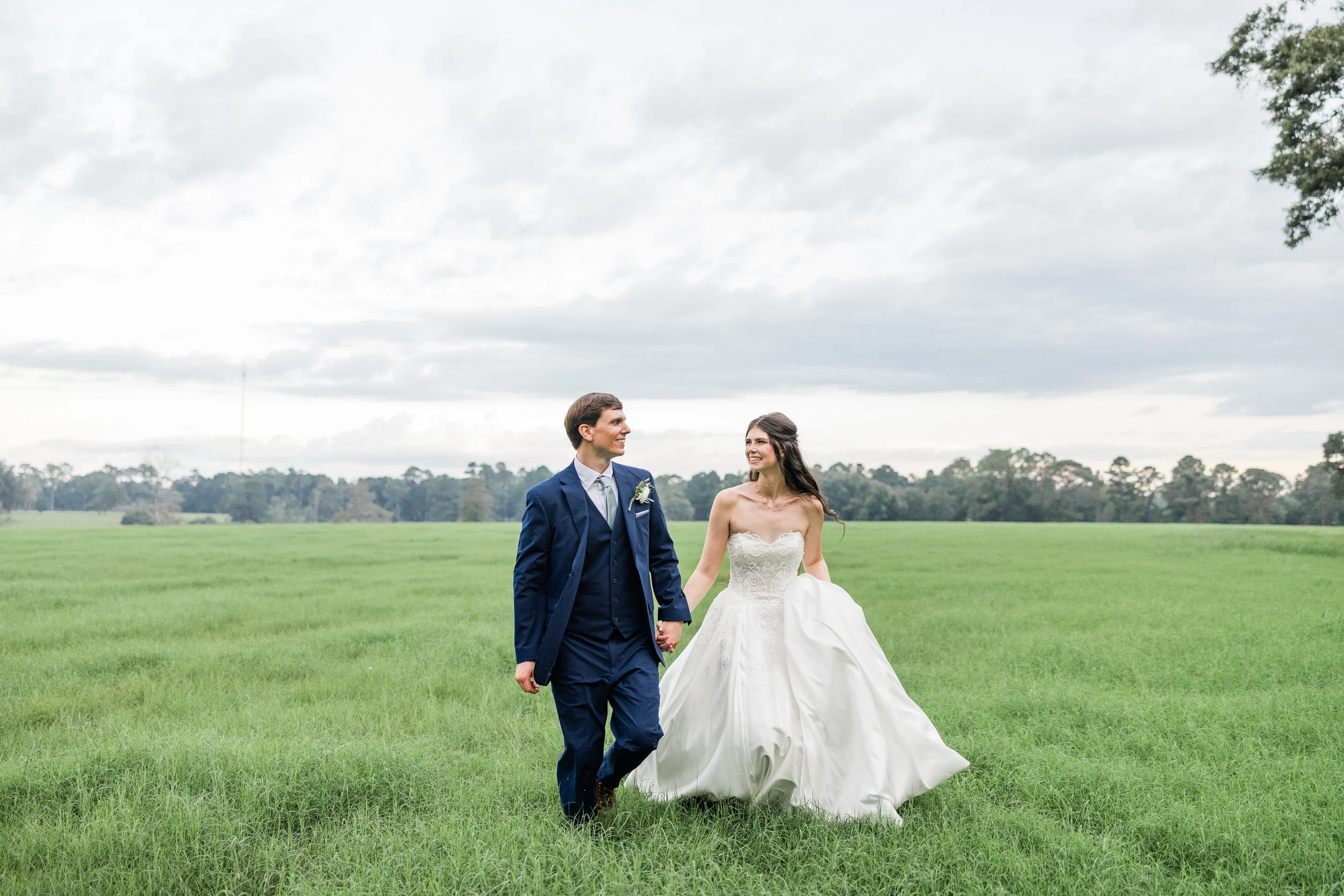 Newlyweds holding hands in a green field, bridal hair and makeup by Briar & Bleu