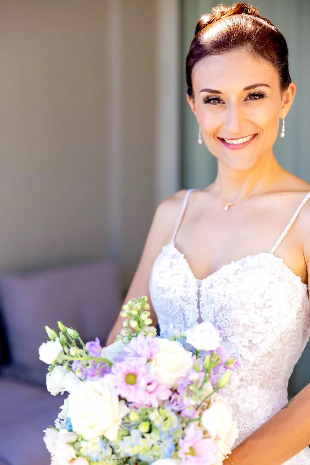A smiling woman in a white lace dress holding a bouquet of multicolored flowers.