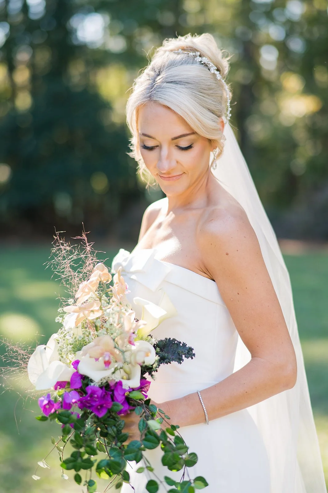 A bride in a white wedding dress holding a colorful bouquet of flowers outdoors with a blurred green background.