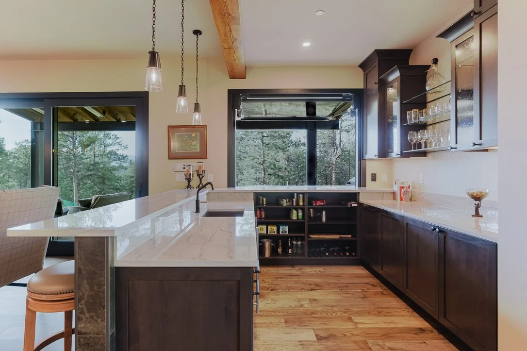 Modern kitchen with dark wooden cabinets, a white marble countertop, and large windows overlooking trees