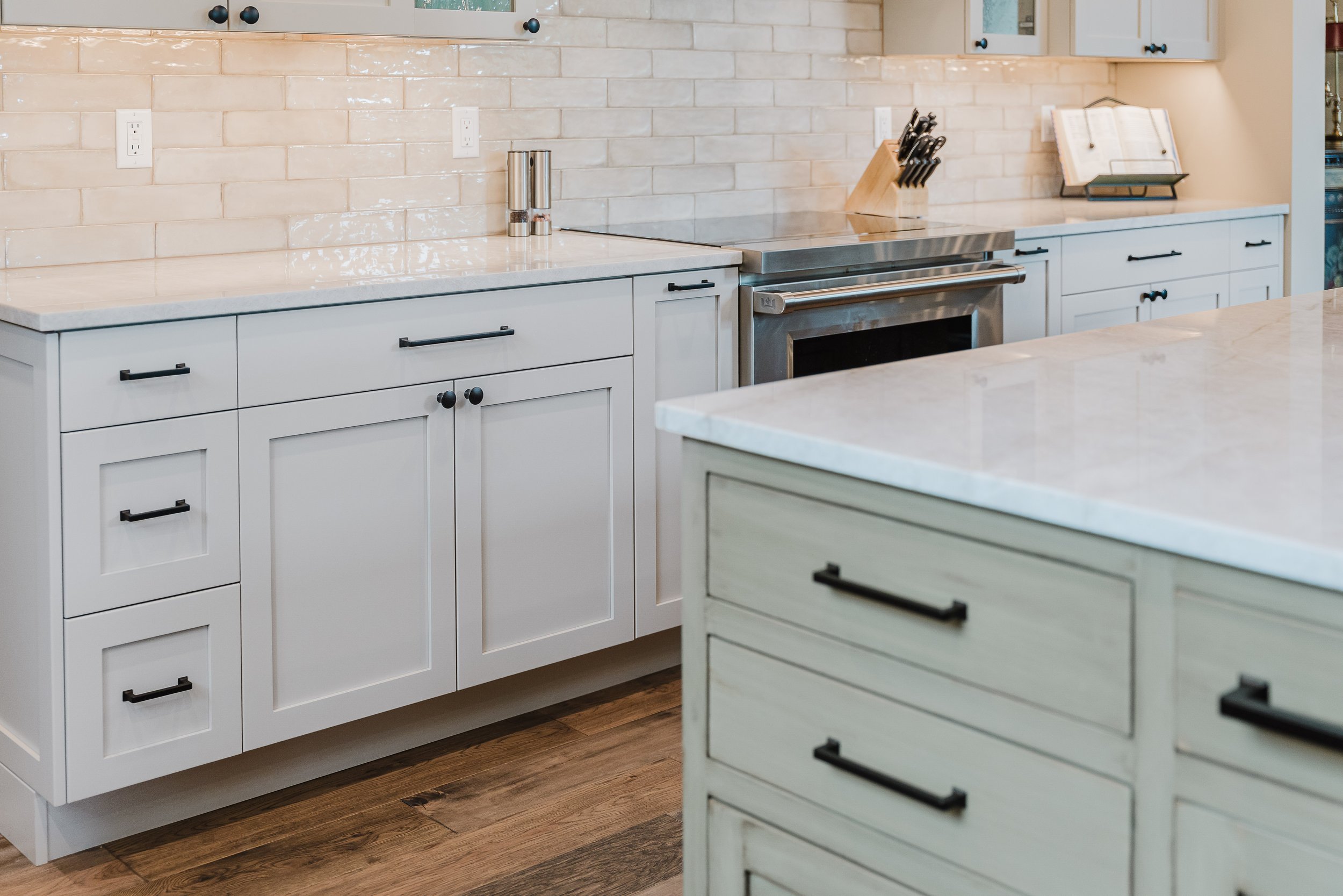 Modern kitchen with white cabinets, a white marble countertop, and a beige tiled backsplash. There is a set of salt and pepper shakers, a knife block, and a paper towel holder on the counter. The kitchen has a stainless steel oven and wooden flooring.