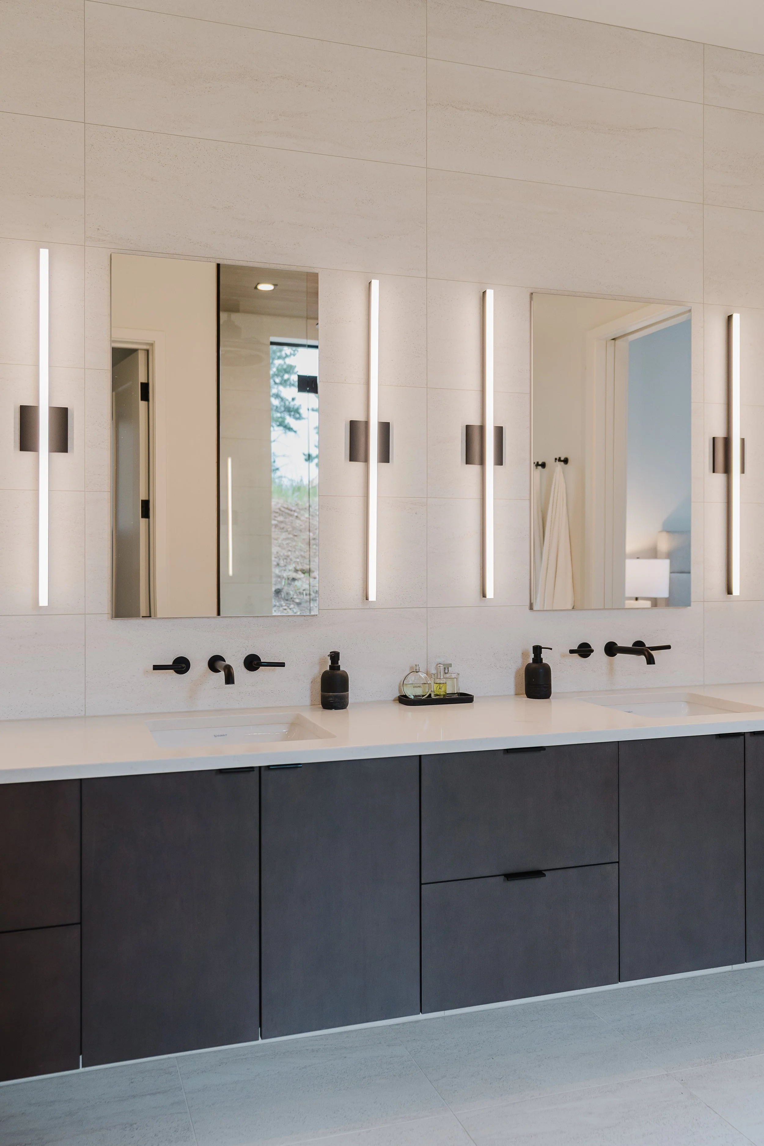 Modern bathroom with two mirrors, black fixtures, black cabinetry, white countertop, and minimalistic decor.