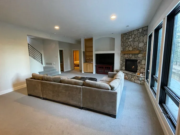 Living room with a large beige sectional sofa, stone fireplace, large windows, and built-in shelves.