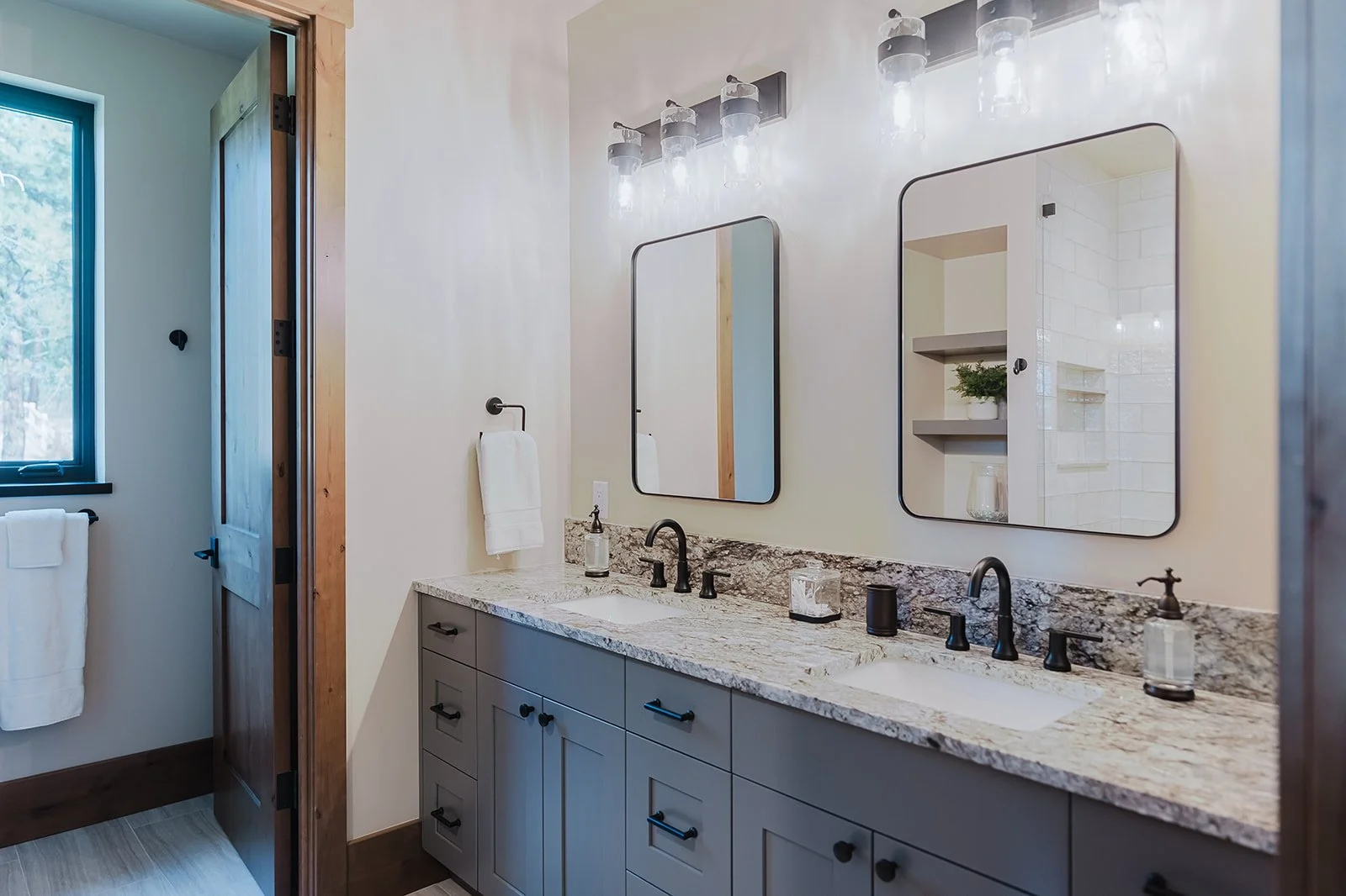 Modern bathroom with double vanity, granite countertop, two mirrors, black fixtures, and a wall-mounted light fixture with multiple bulbs.