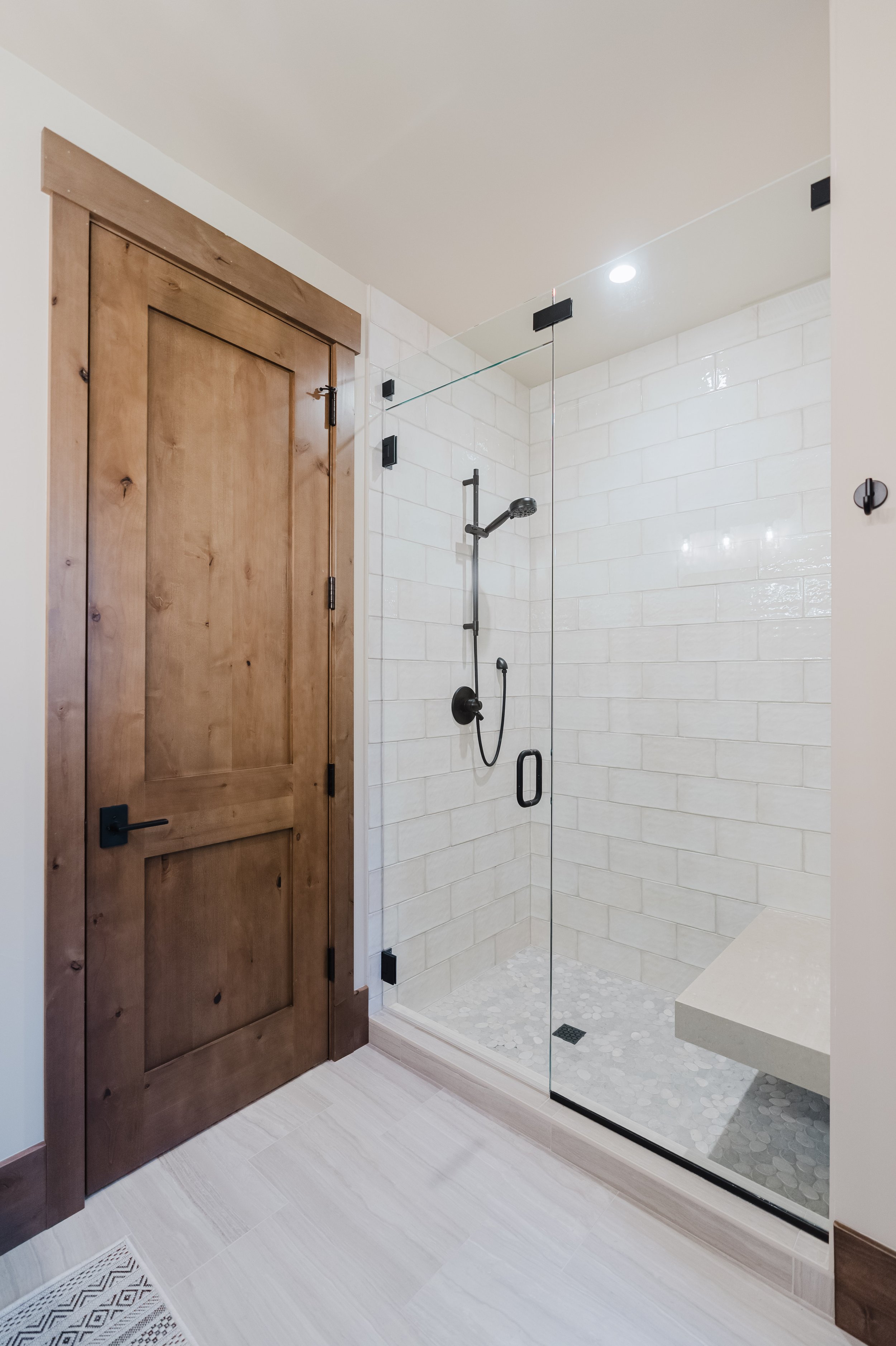 Modern bathroom with a glass shower enclosure, white subway tile walls, and wooden door with black hardware.