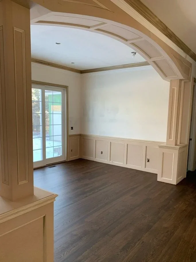 Empty dining room with hardwood flooring, beige wainscoting, large window with a sliding glass door, and intricate ceiling molding.