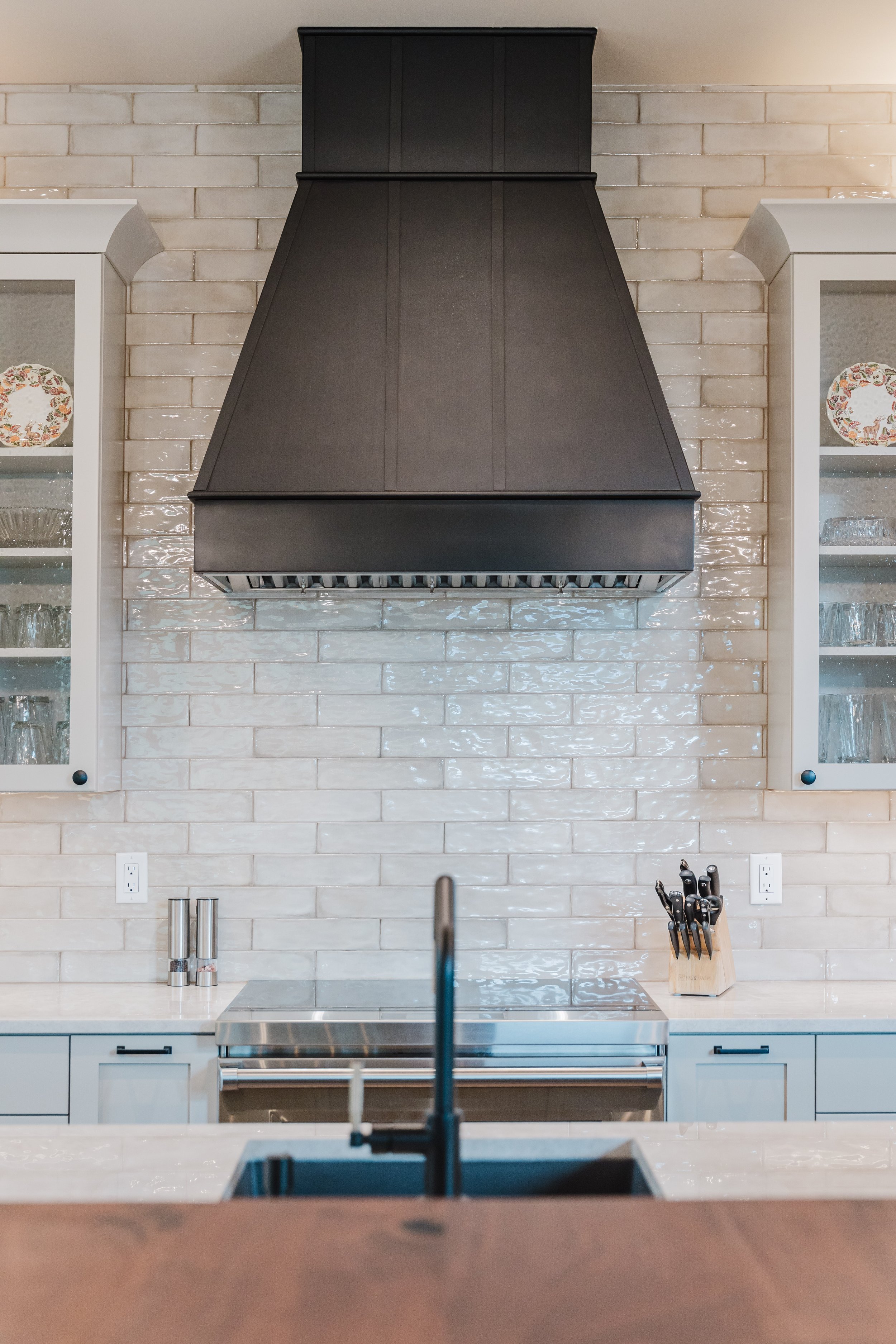 Kitchen with white cabinets, a black range hood, a white tiled backsplash, and a kitchen knife block on the counter.