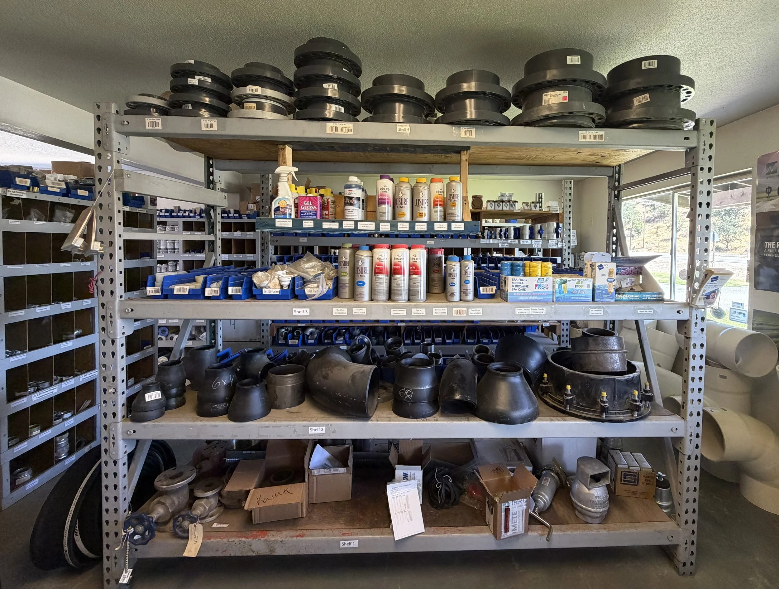 Shelves with pool equipment including hoses, filters, and parts in a storage room.