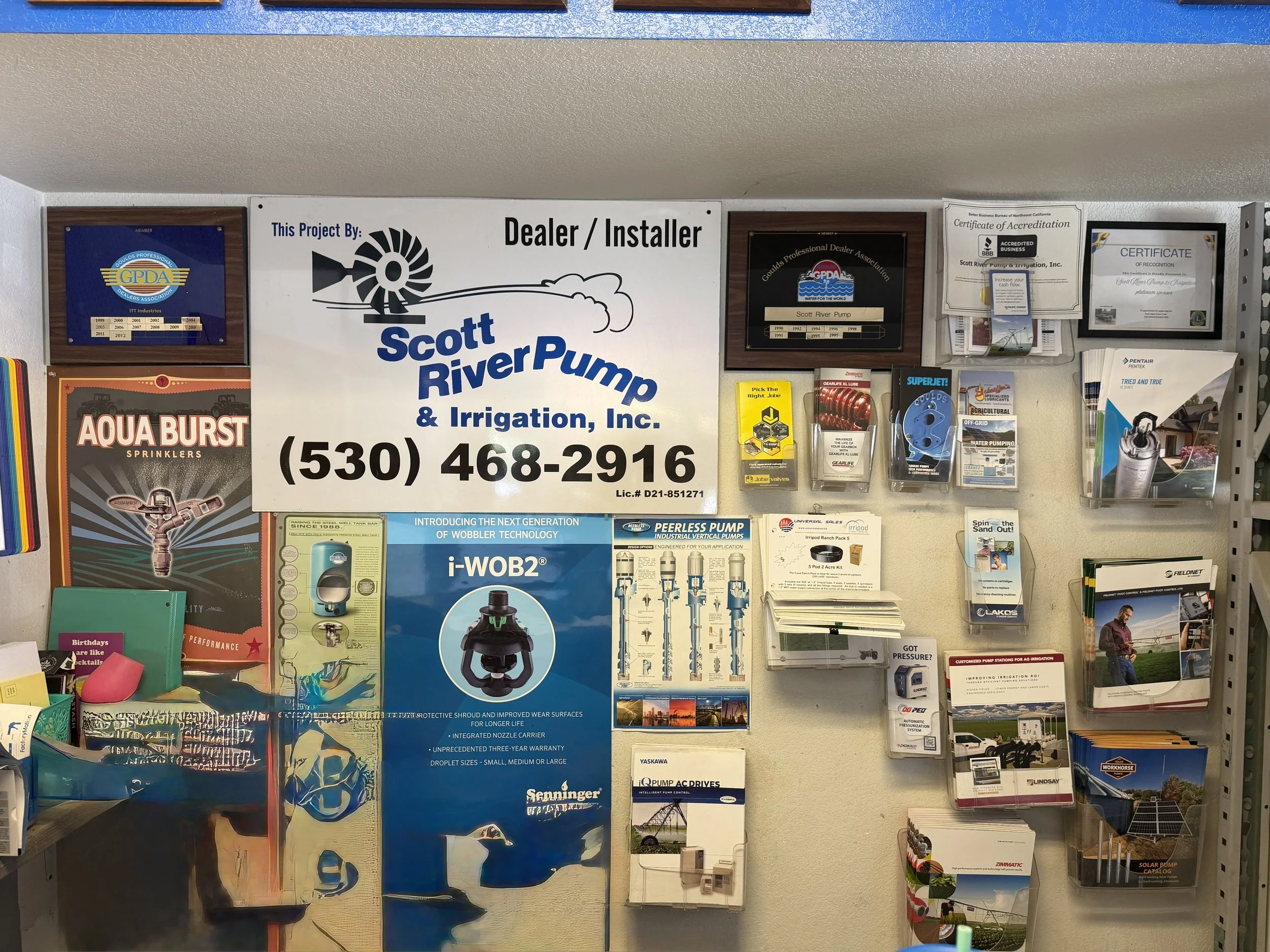 A display of various HVAC and irrigation product brochures and certificates, including a large sign for Scott River Pump and Irrigation, Inc., with contact information and product details, along with awards and certifications mounted on the wall.