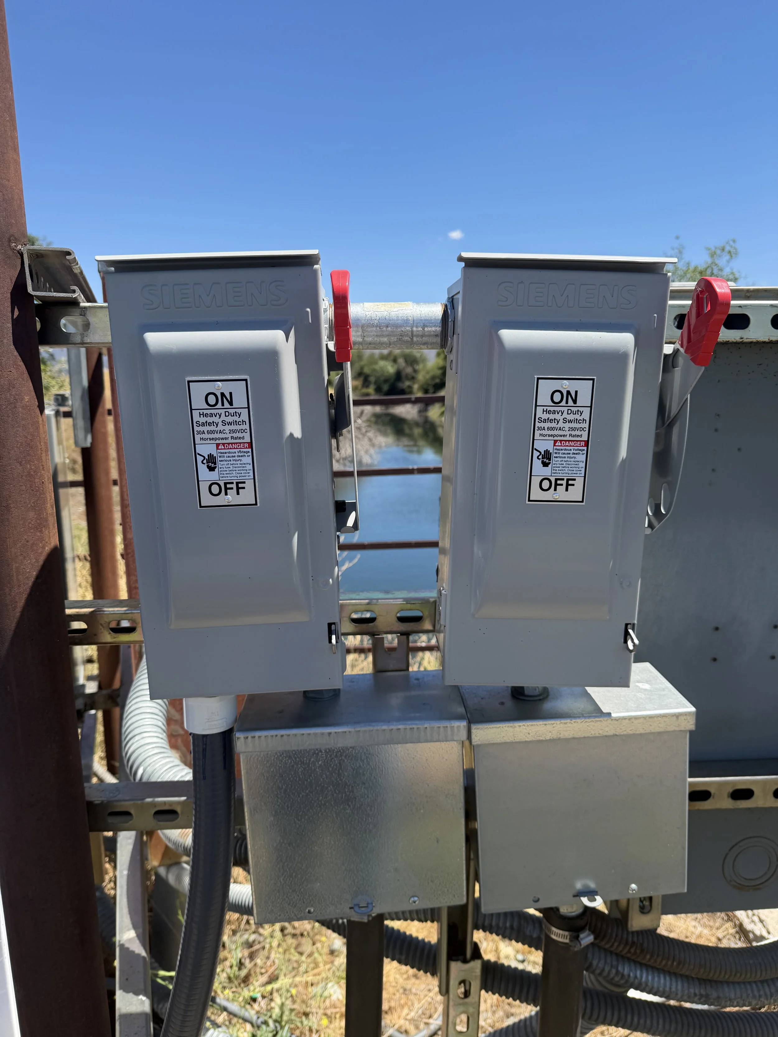 Close-up of electrical safety switches labeled Siemens, mounted on a metal box outdoors, with blue sky and water in the background.