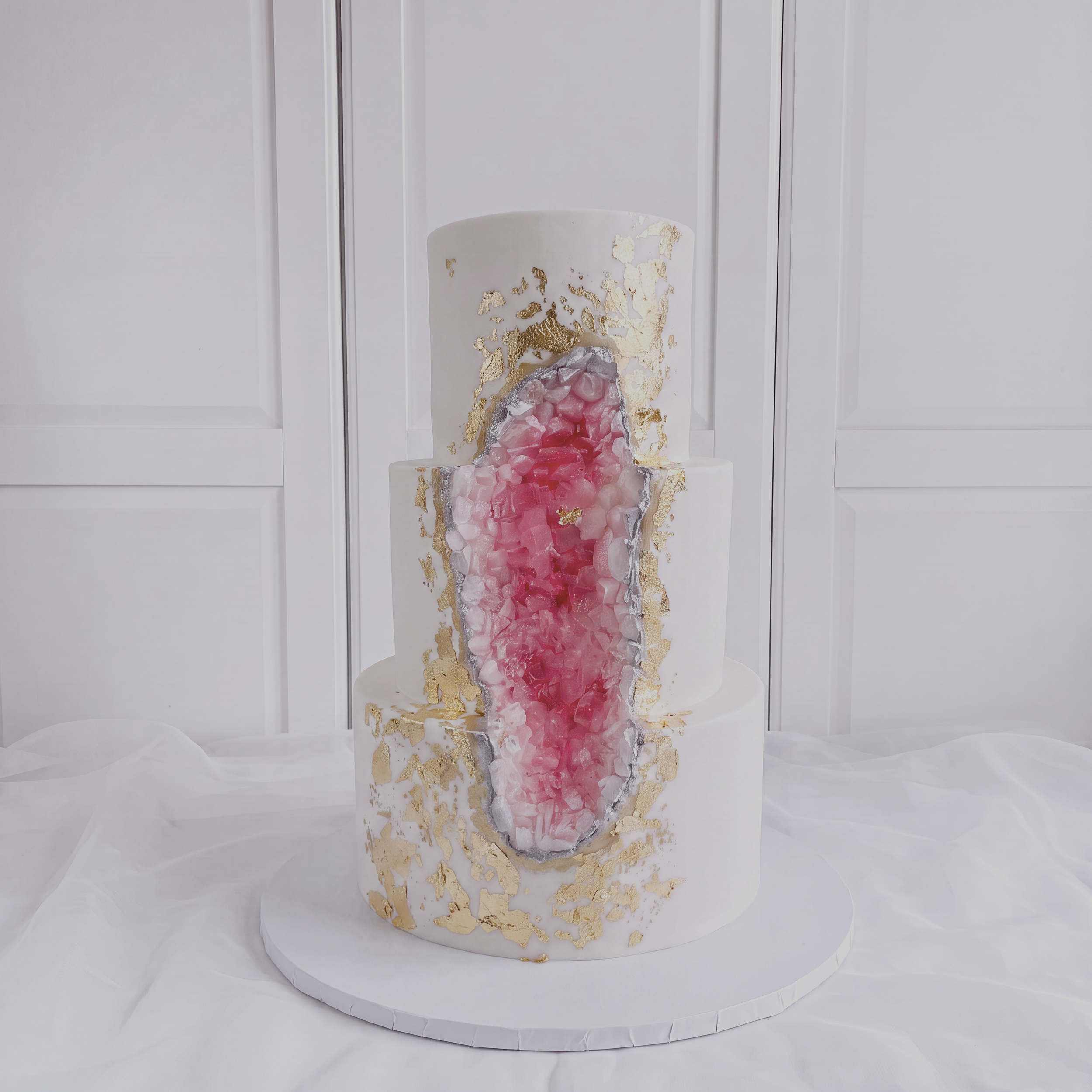 A 3 tier custom wedding cake with pink and white stones, gold accents and silver details.