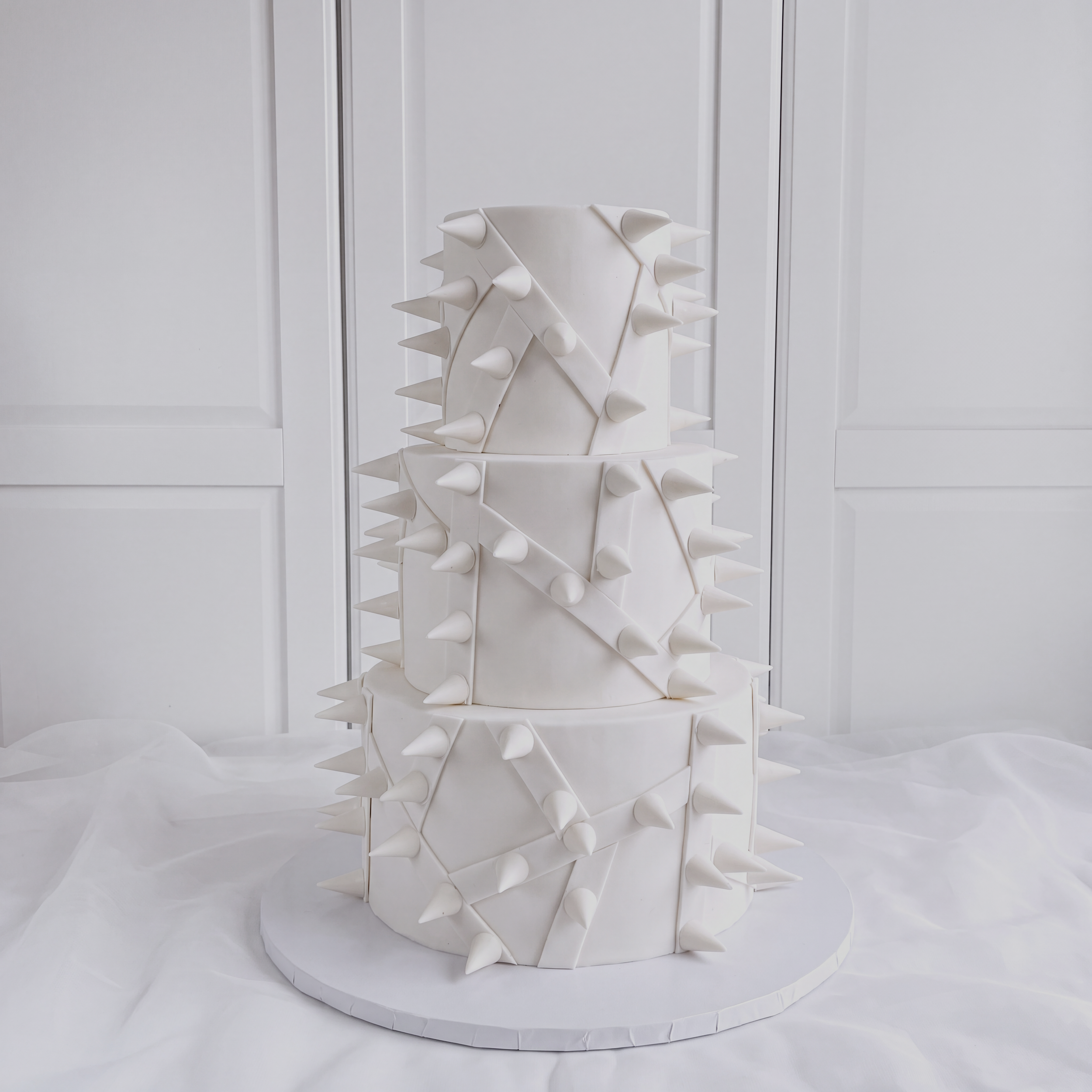 A 3 tier white wedding cake decorated with large white spikes made out of chocolate. Not the traditional cake for a wedding.