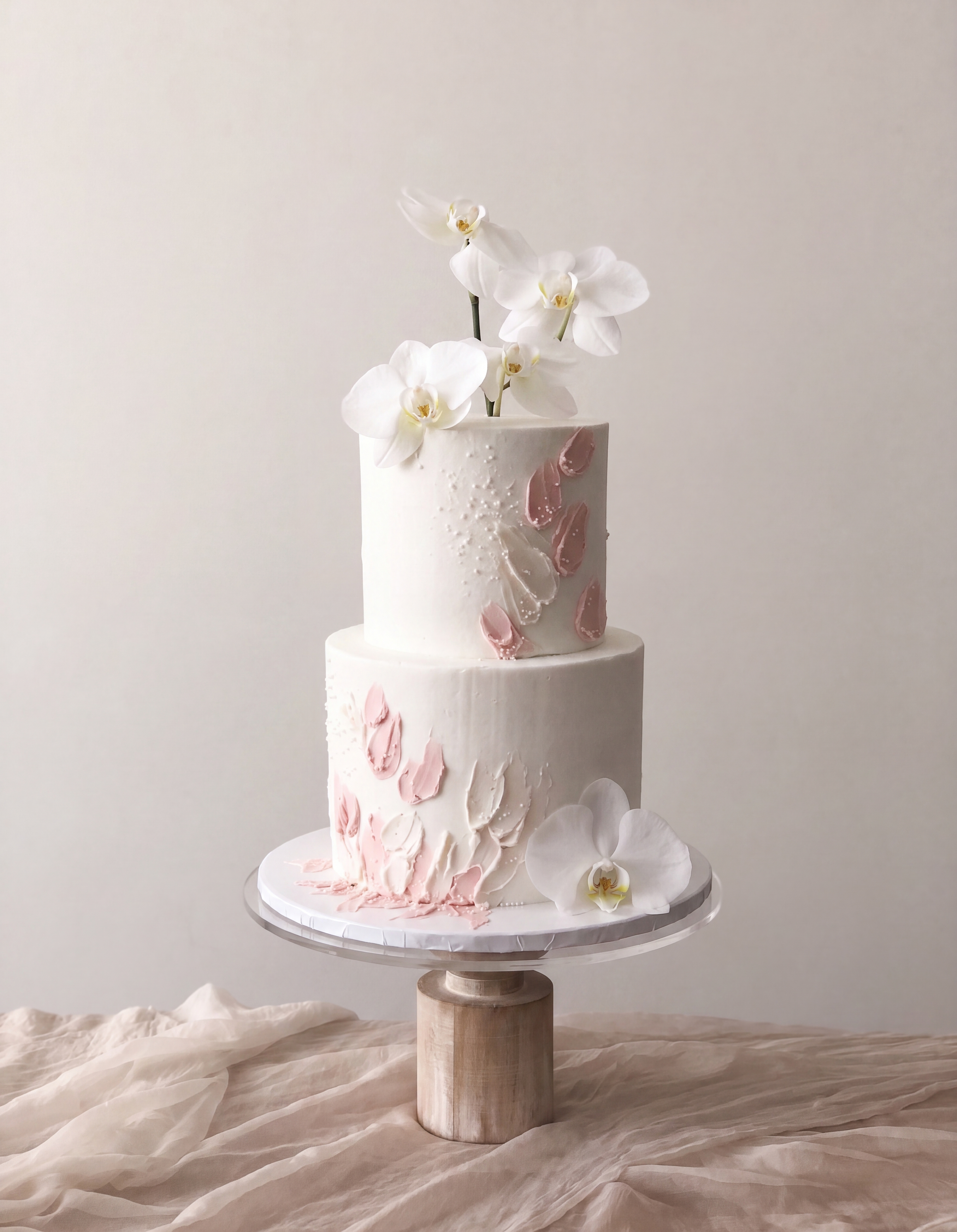 A tall, multi-layered white cake decorated with white orchids and pink and white buttercream embellishments.