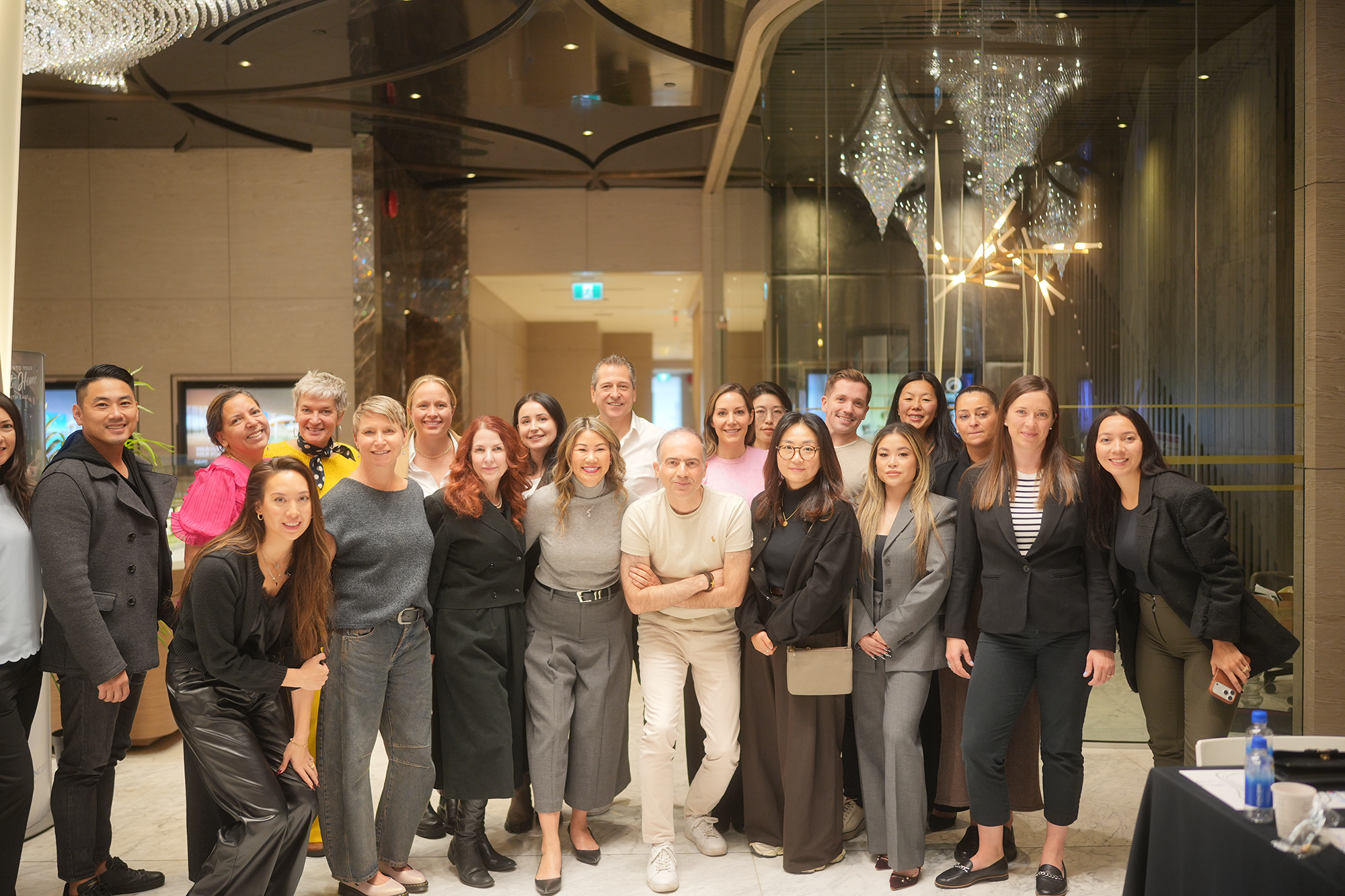 Group of diverse people standing together in a hotel lobby, smiling at the camera, at a social event or gathering.