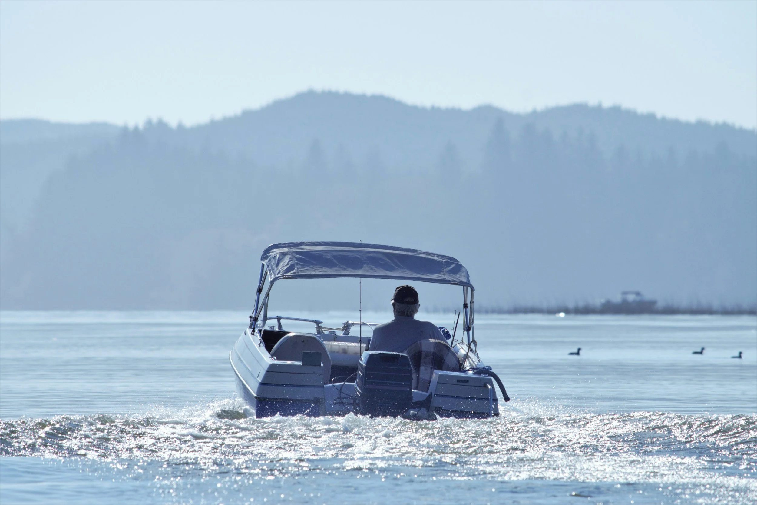 A person in a boat on a body of water with a mountain range in the background.