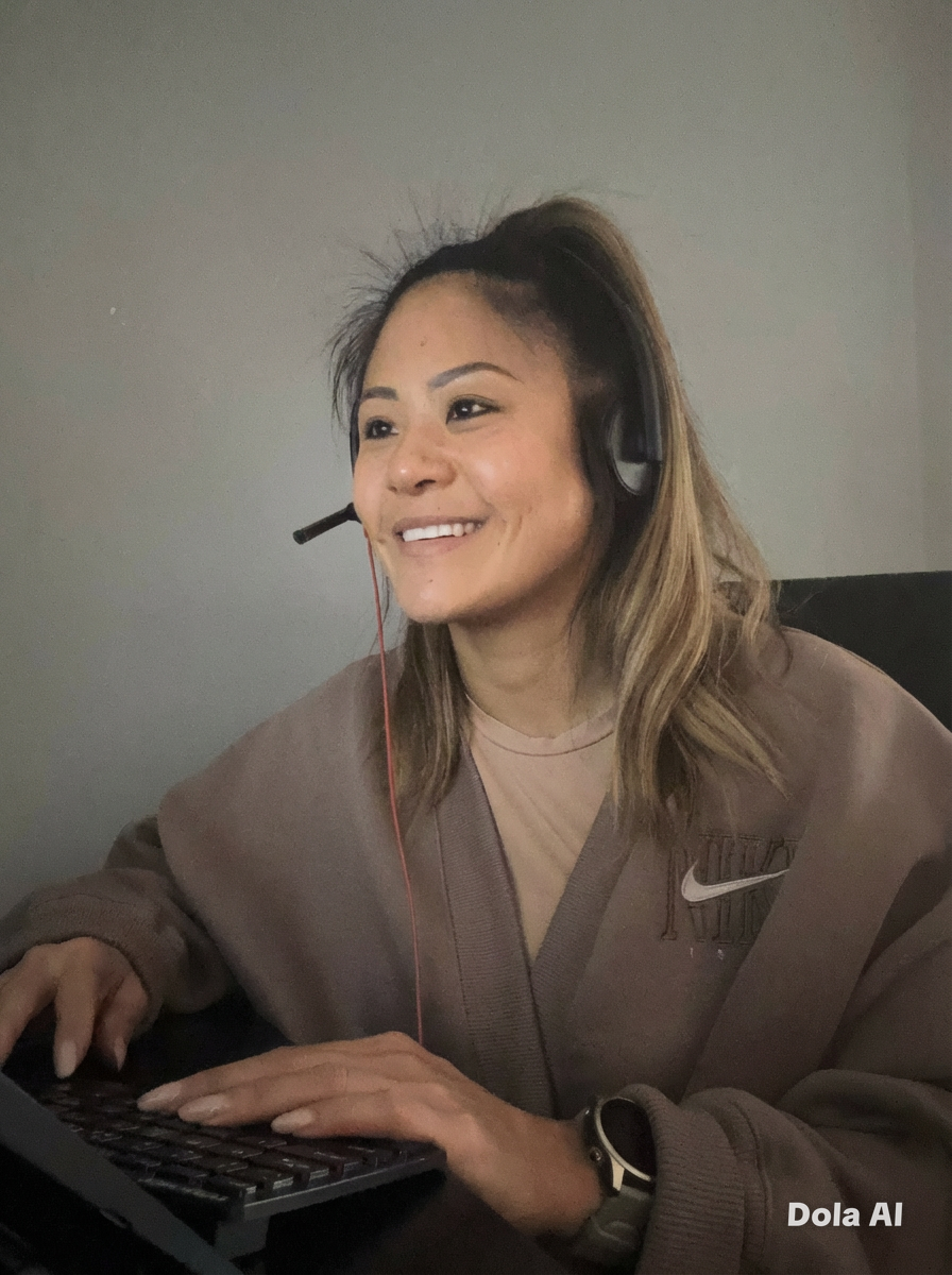 A woman with long, wavy hair wearing a headset, smiling while working on a computer.