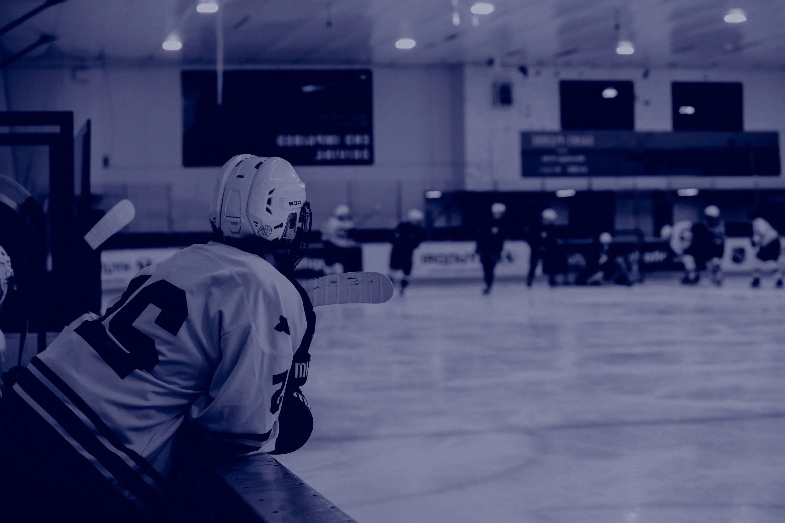 hockey player leaning over side of the rink watching teammates play