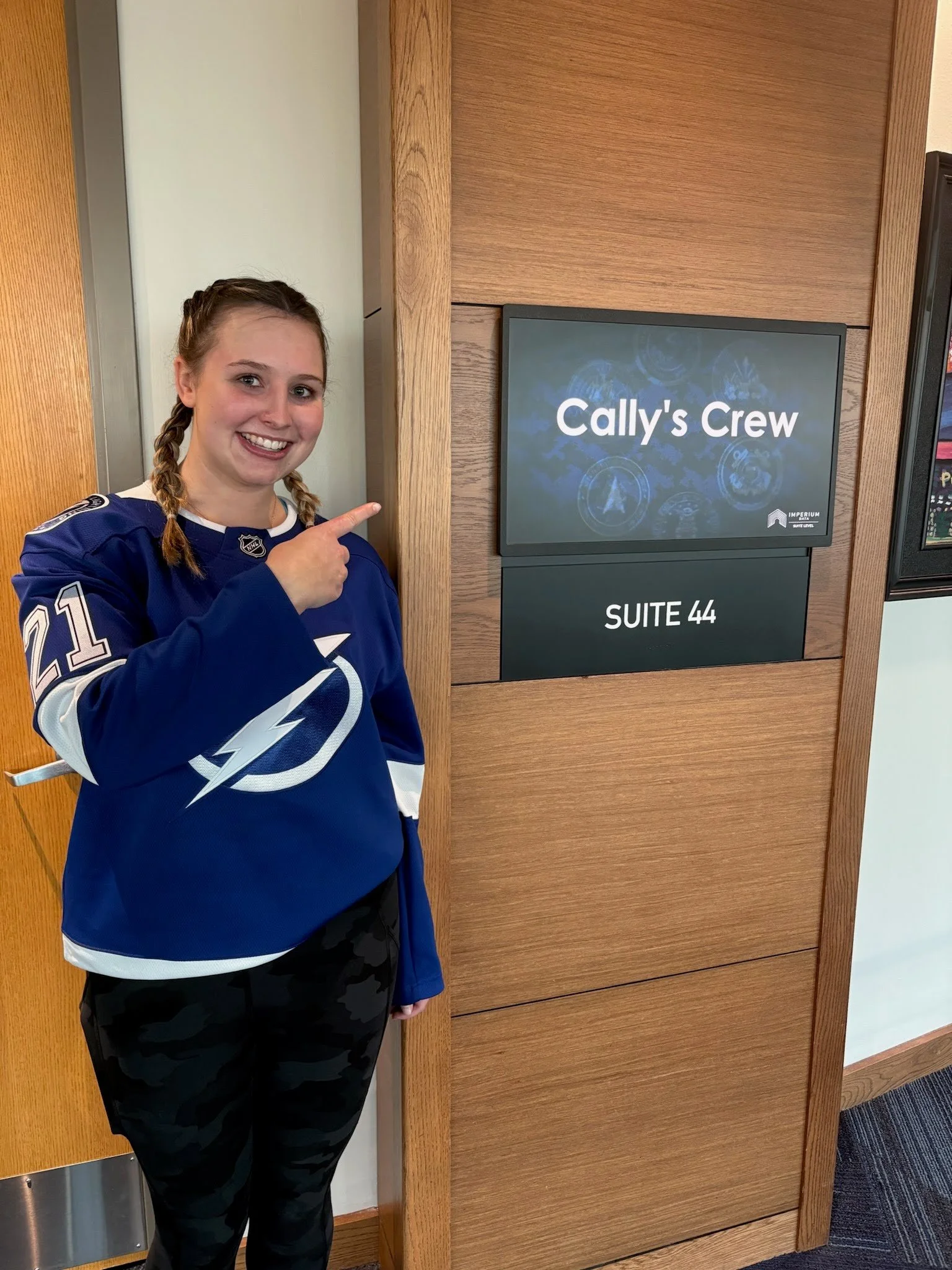 teenage girl wearing a hockey jersey posing in front of the Cally's Crew game suite