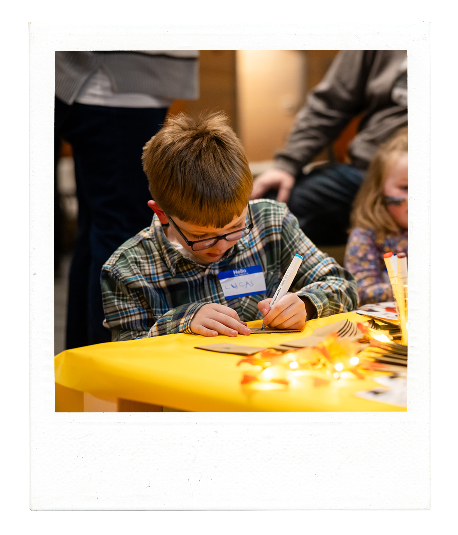 young boy with glasses in a plaid shirt sitting at a yellow table drawing during a Friendsgiving charity event