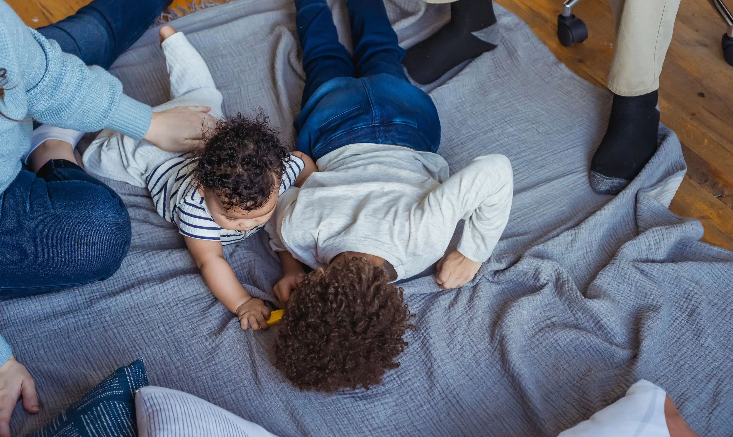 two siblings joyfully playing on a blue blanket surrounded by their parents