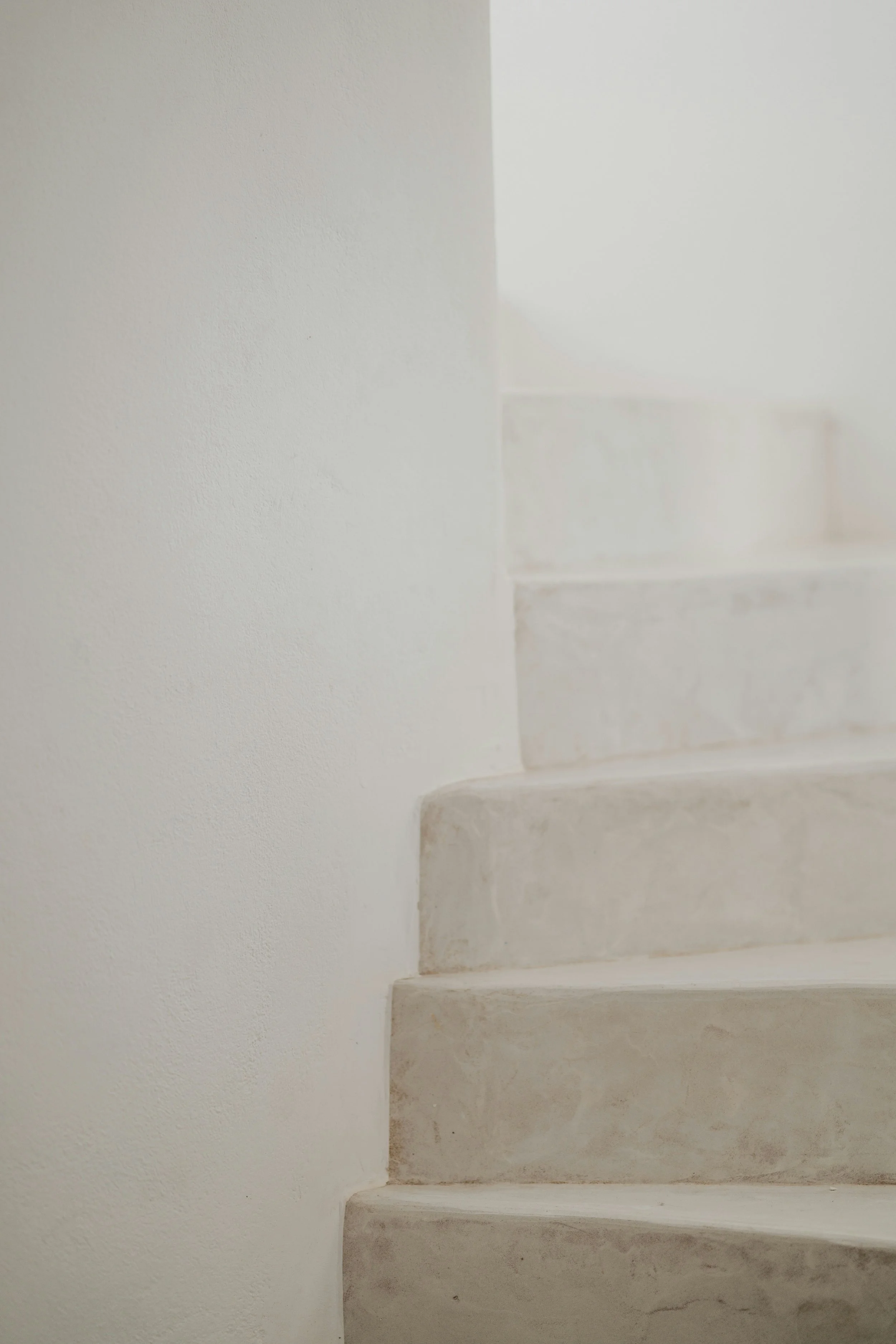 Close-up of a section of beige concrete stairs with a white wall on the left side and soft, natural light.