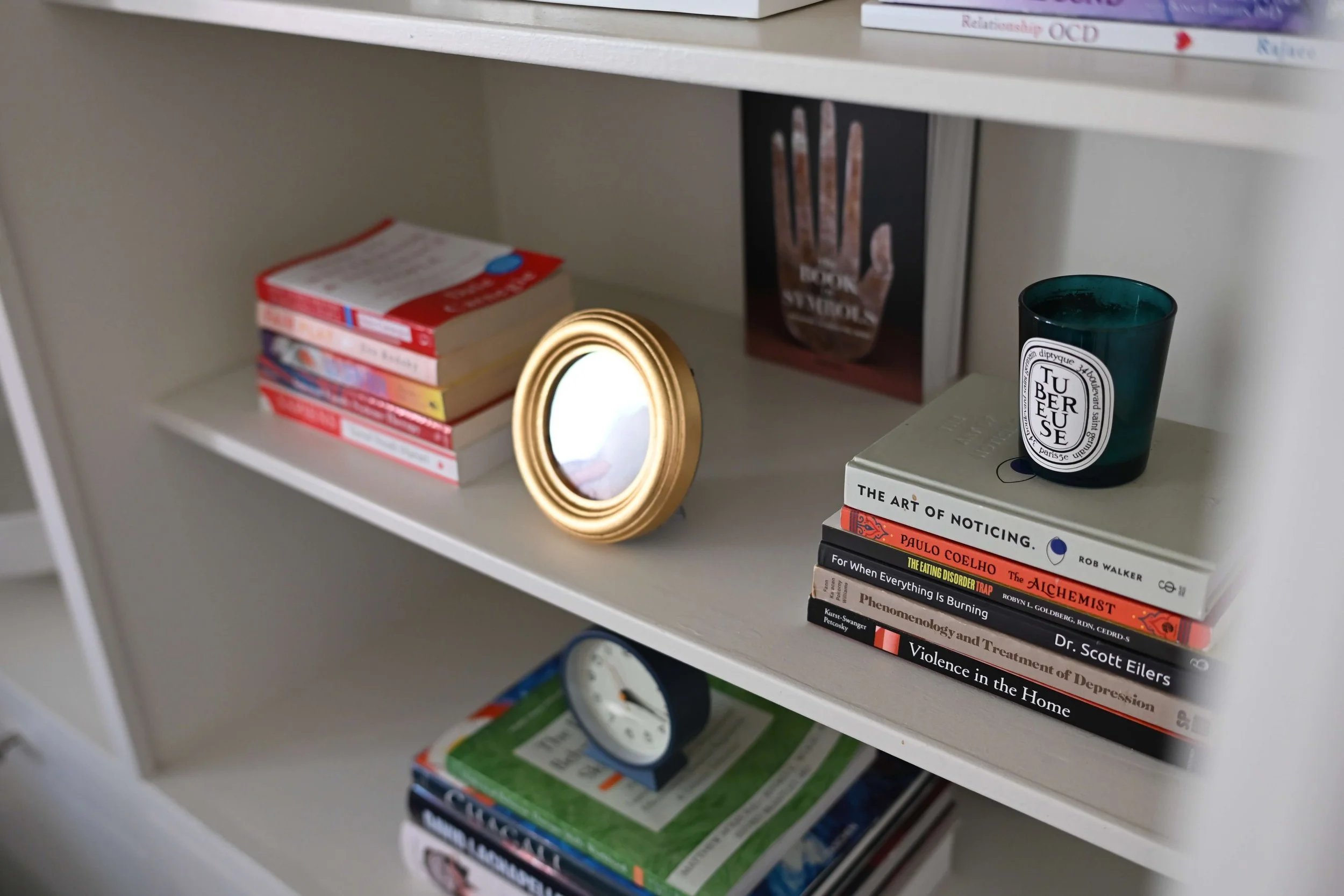 Bookshelf with various academic and self-help books, a small mirror, a candle in a glass container, and a magazine page with a hand on black background.