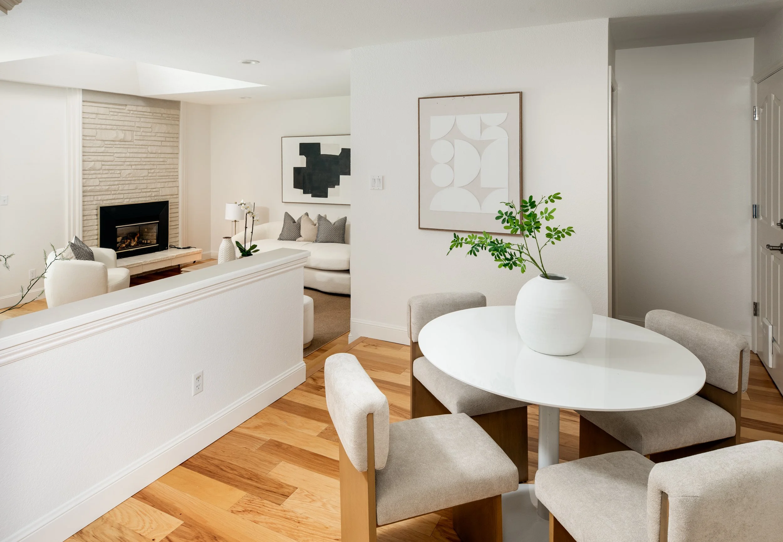 A modern living room with a white sofa, black and white pillows, a fireplace, artwork on the walls, and a small potted plant in a white vase on a table.