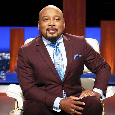 Man in a maroon suit with a blue tie sitting in a television studio