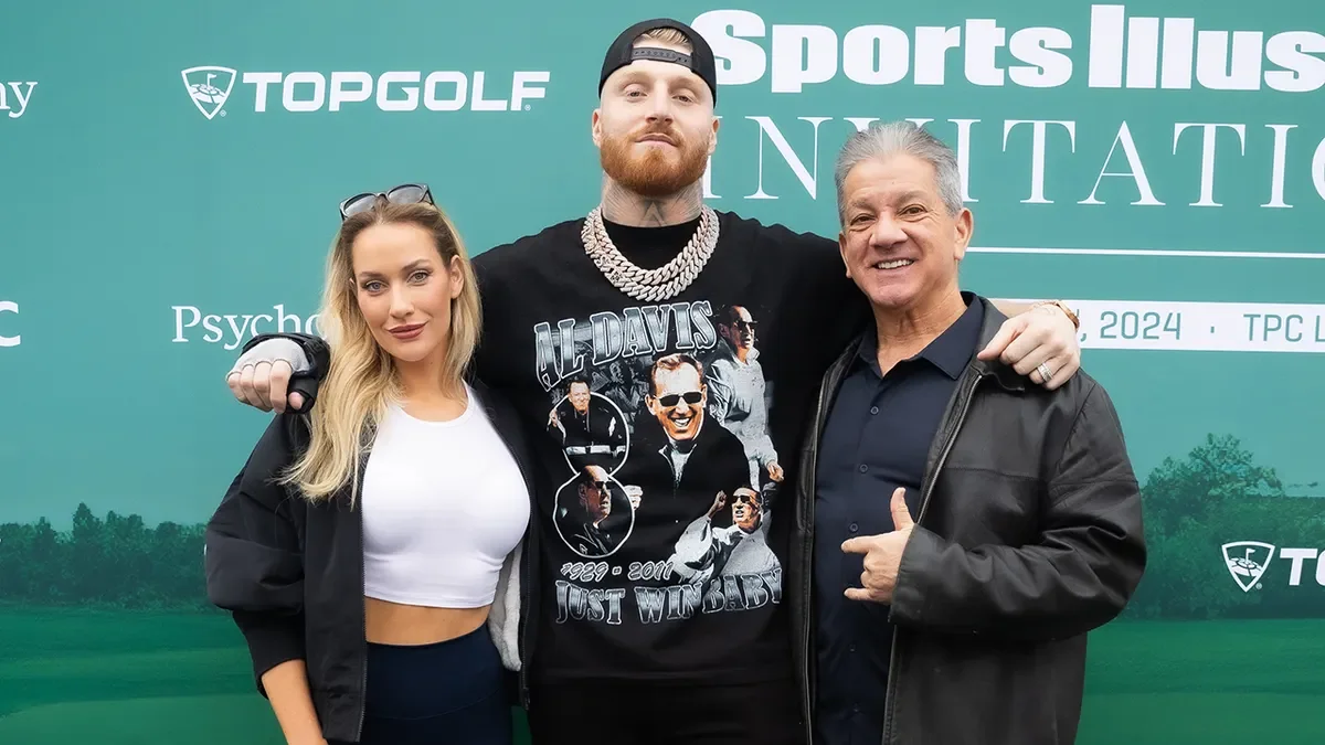 Three people standing together at a golf event, smiling, with a green backdrop displaying the logos "Topgolf" and "Sports Illustrated".