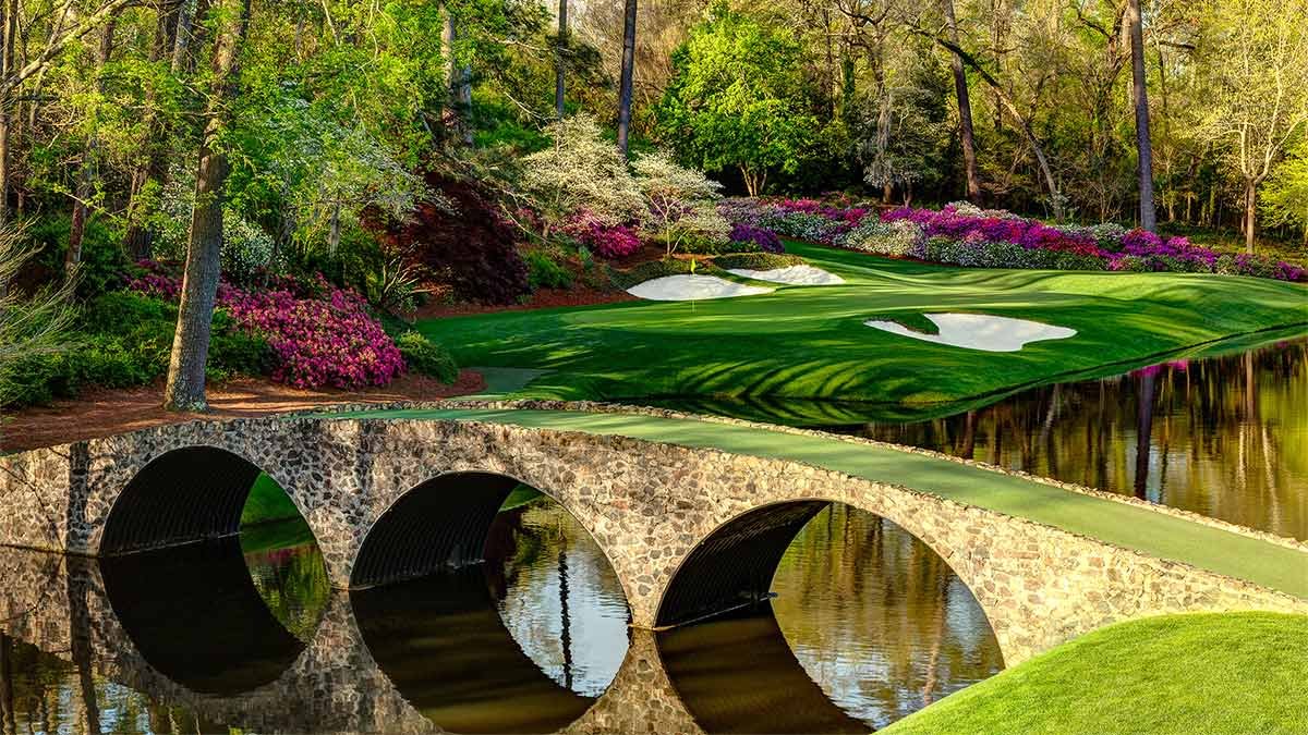 Scenic landscape with a stone bridge over water, surrounded by blooming flowers and lush green trees.