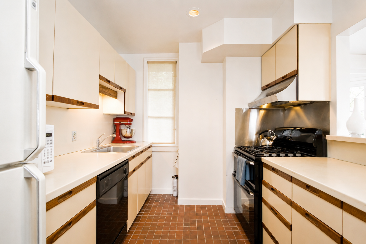 Kitchen with beige cabinets, brown trim, white countertops, a red stand mixer, a black oven and stove, and brown tiled floor.