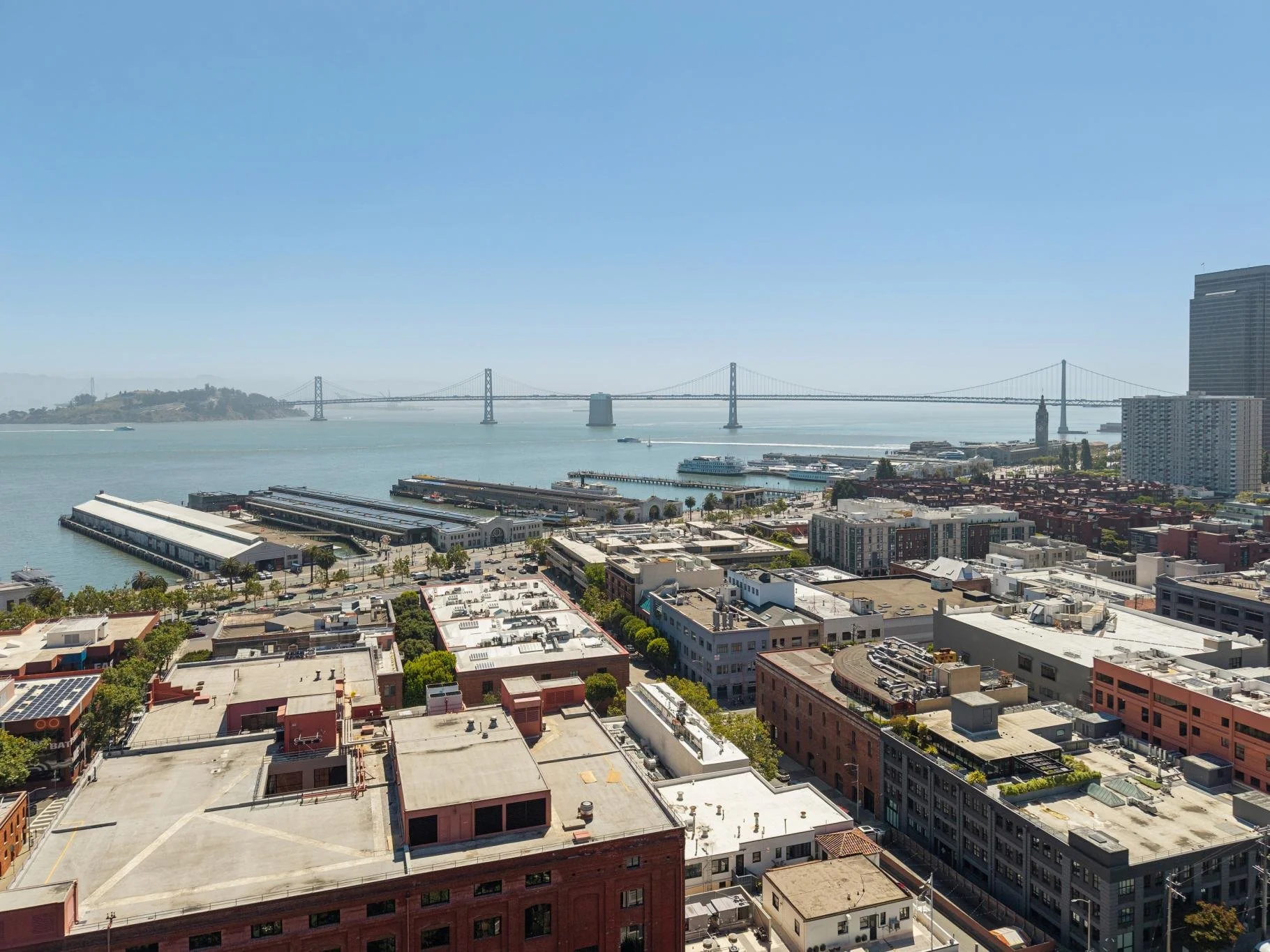 Cityscape view of San Francisco with the Bay Bridge, buildings, and water in the background, under clear blue skies.