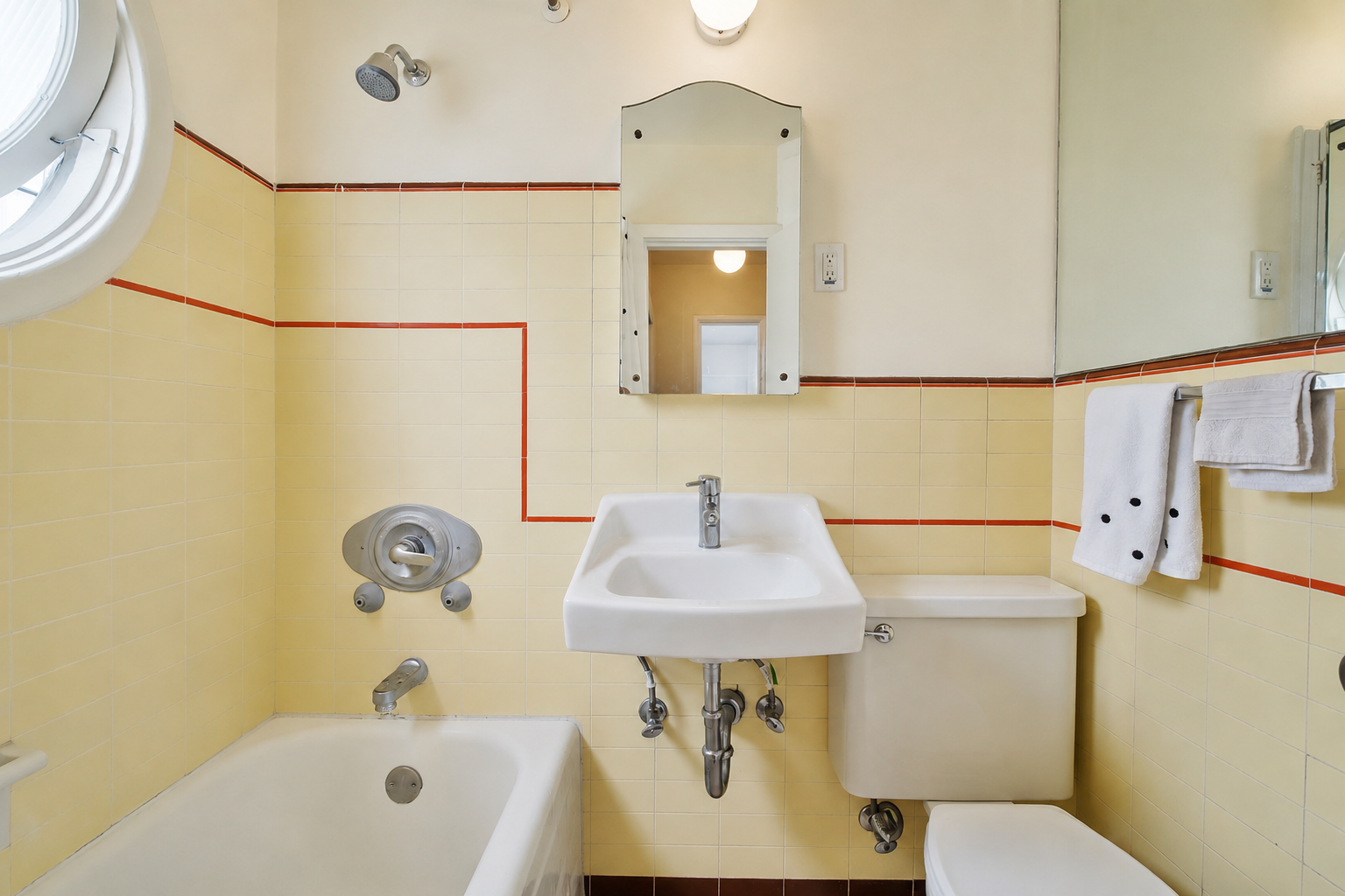 Small bathroom with yellow tiled walls, a bathtub, a wall-mounted sink, a mirror, and towels on a rack.