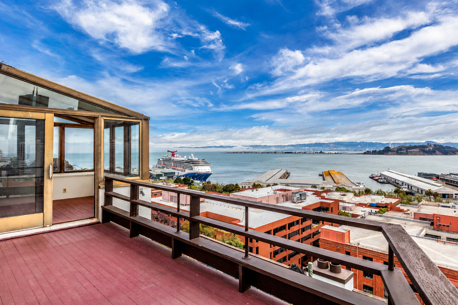 Balcony view overlooking a bay with cruise ships, buildings, and hills under a partly cloudy blue sky.