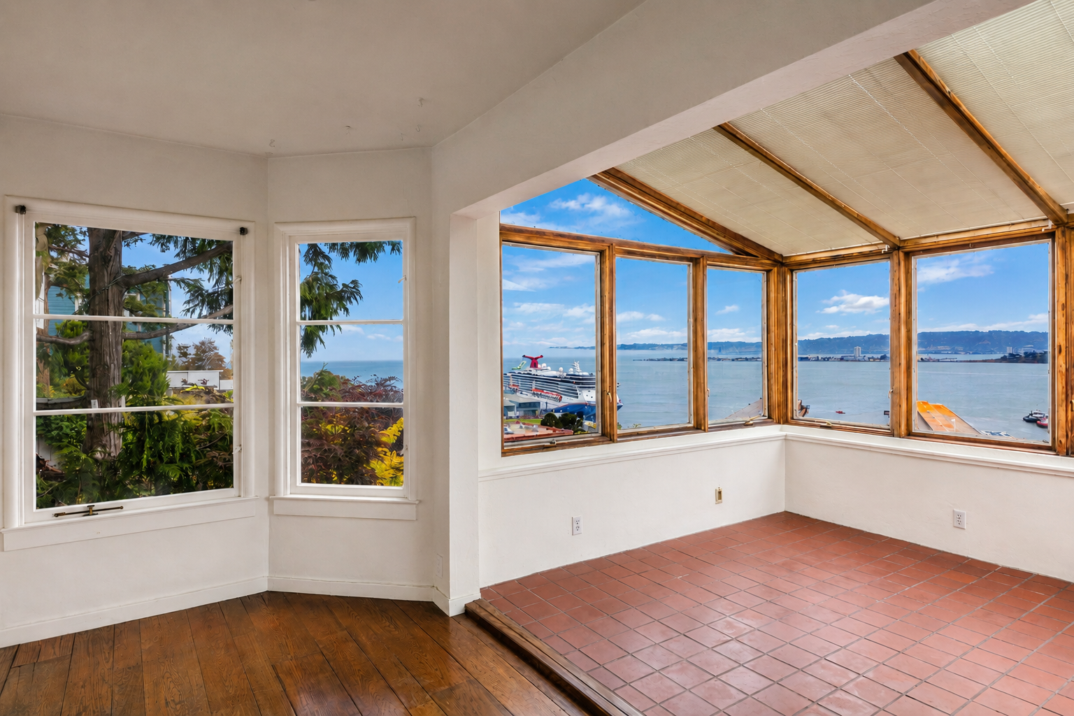 Room with large windows overlooking a harbor with ships and mountains, sunlight streaming in.