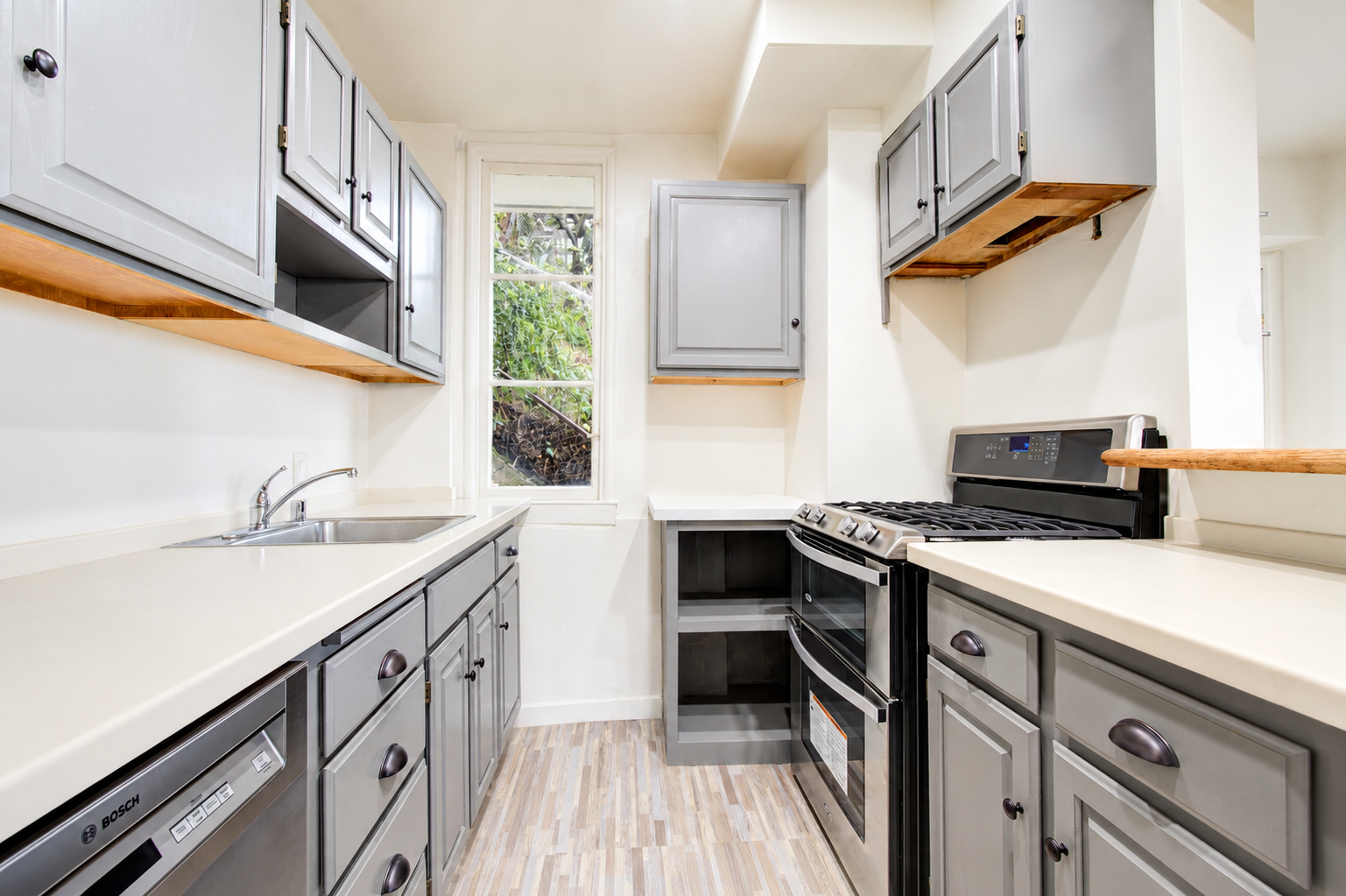Small kitchen with gray cabinets, white countertops, a window with greenery outside, a stainless steel oven, and a dishwasher.