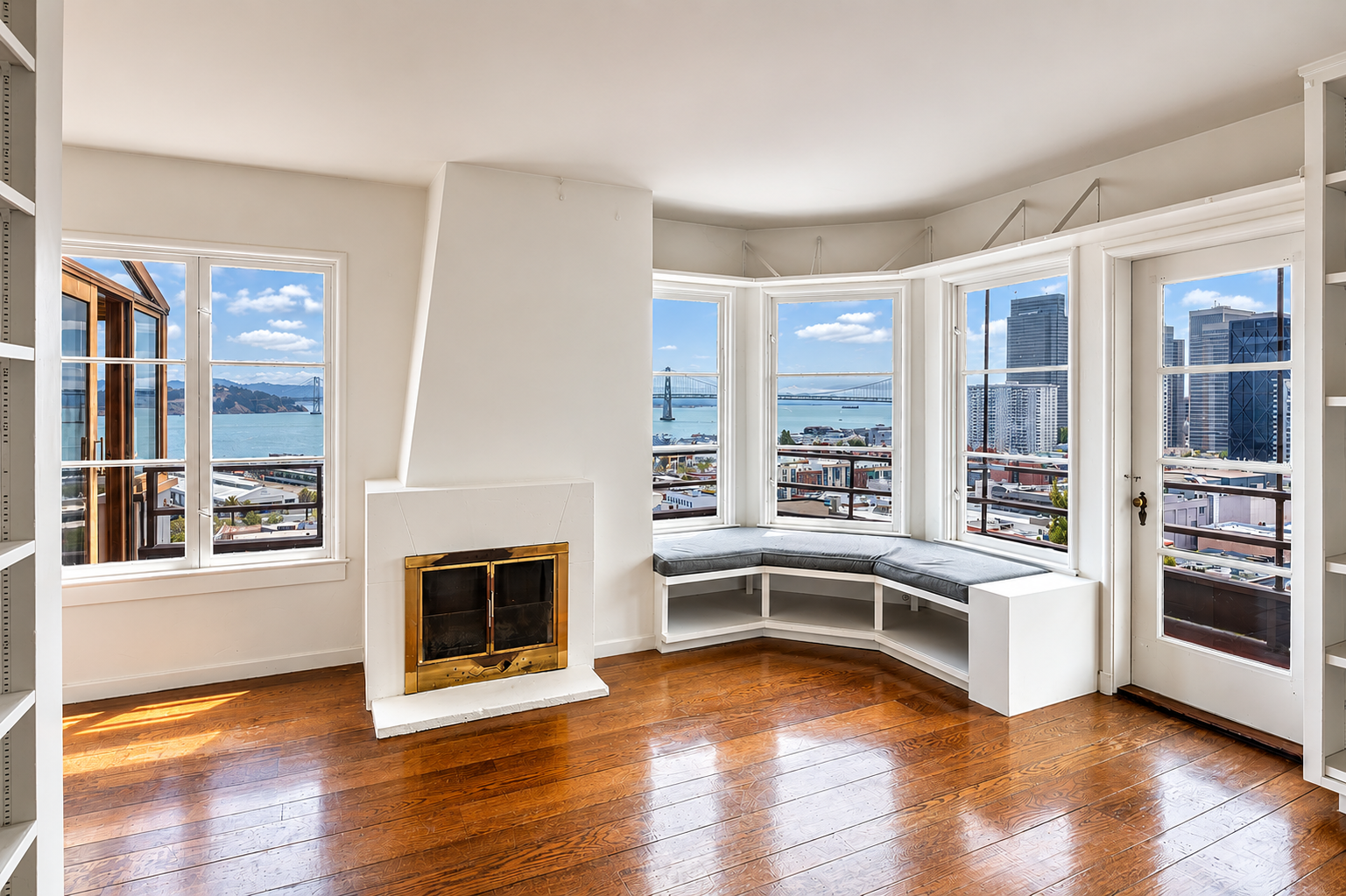 Bright living room with large windows offering a city and bay view, a white fireplace, and a built-in window seat with a black cushion.
