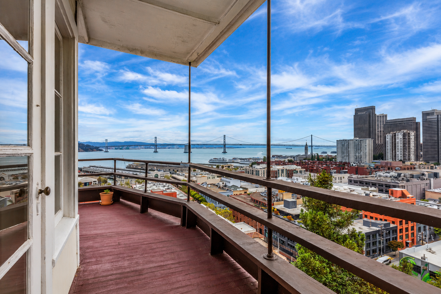 View from a balcony overlooking a city skyline, a bay, and a bridge with a partly cloudy blue sky.