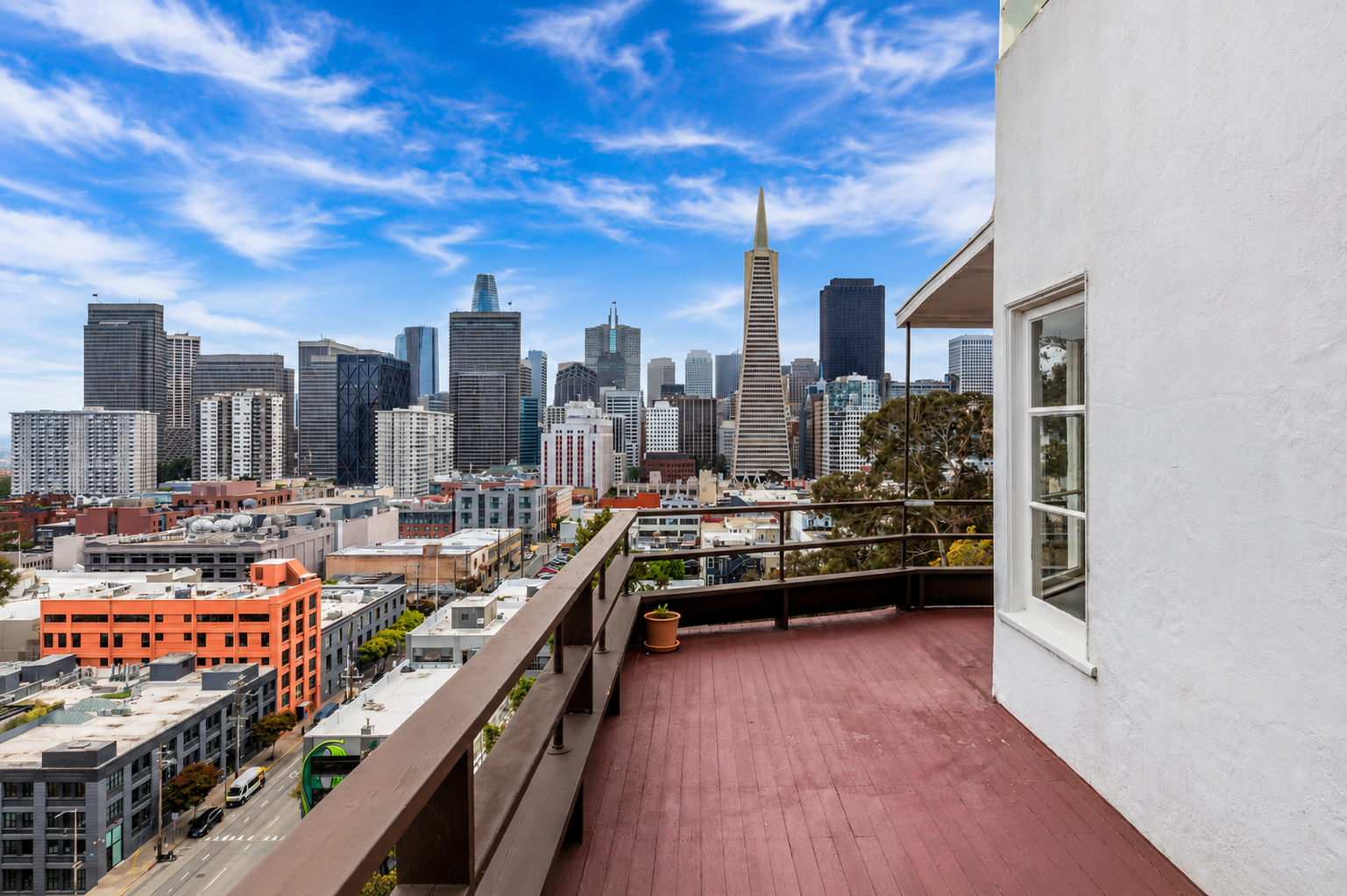 View from a balcony in San Francisco showing city skyscrapers, including the Transamerica Pyramid, with a partly cloudy blue sky.