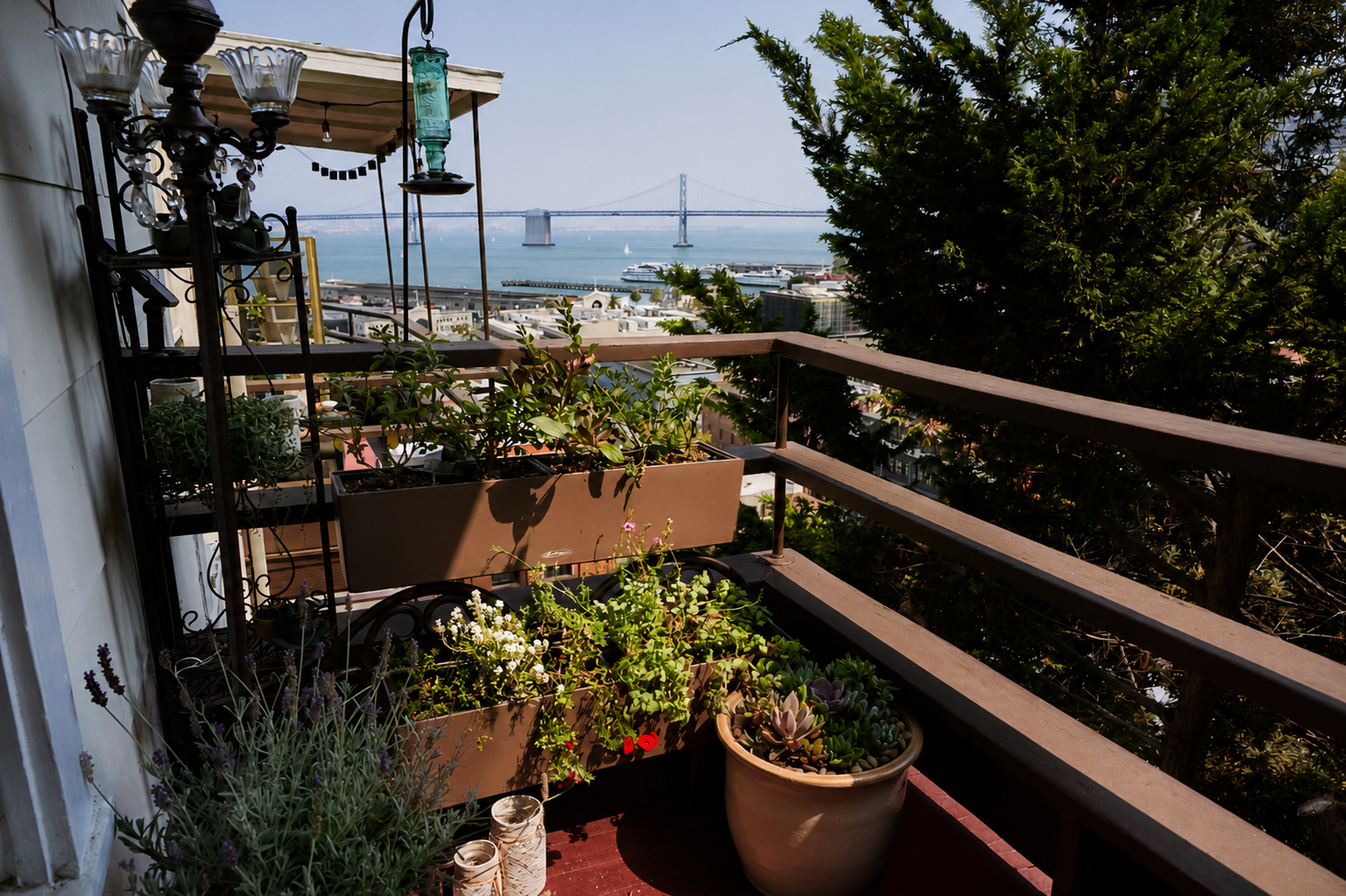 View of a balcony with potted plants and a cityscape in the background, including a bridge over a body of water and boats.