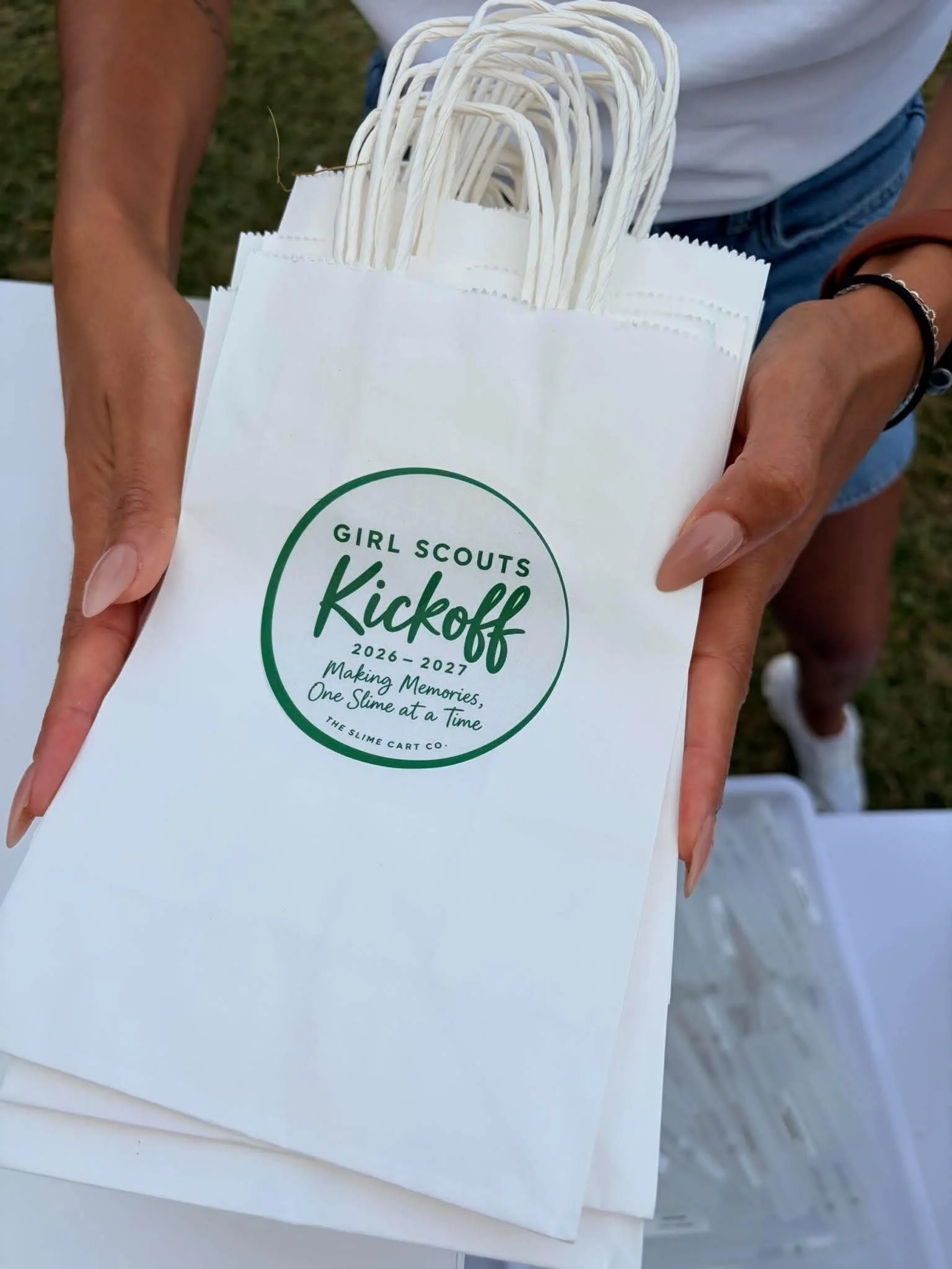 Hands holding white bags with a Girl Scout kickoff meeting logo