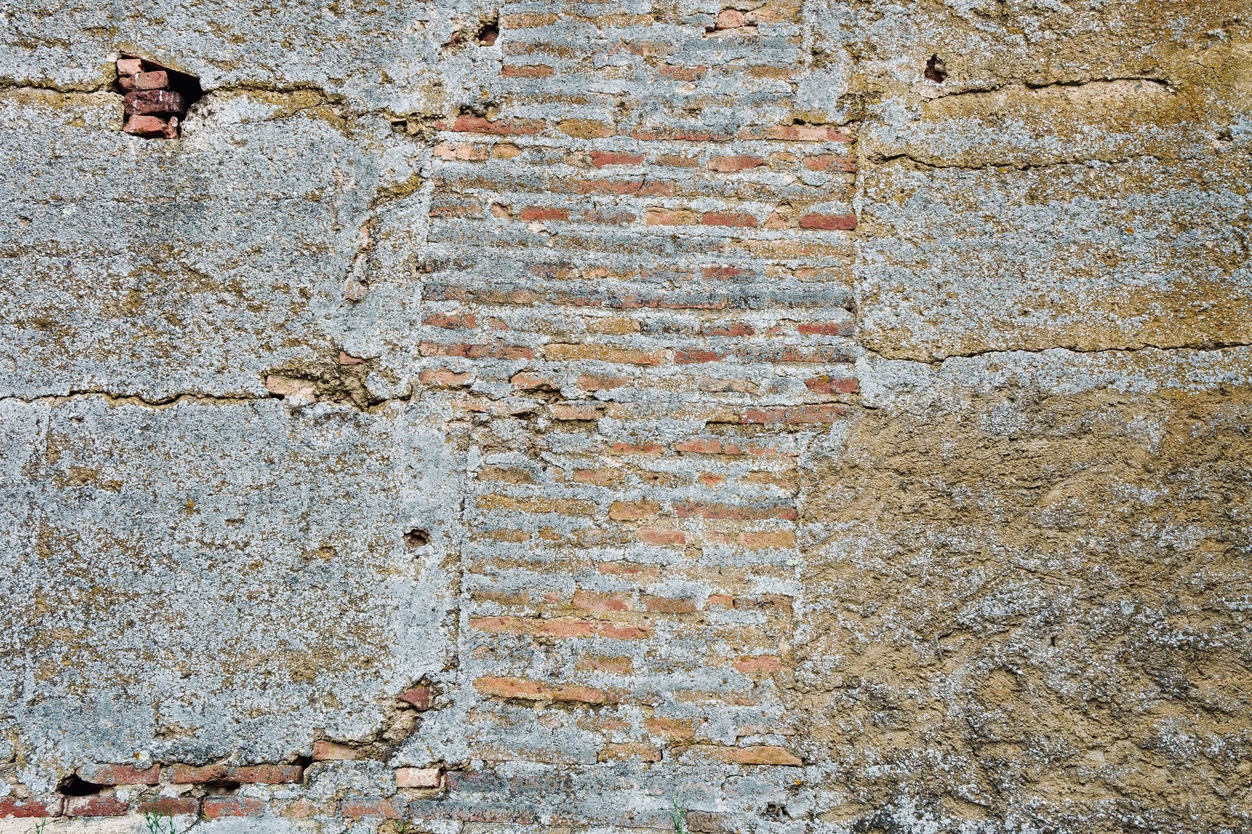 Close-up of a weathered brick wall with peeling concrete and visible cracks.