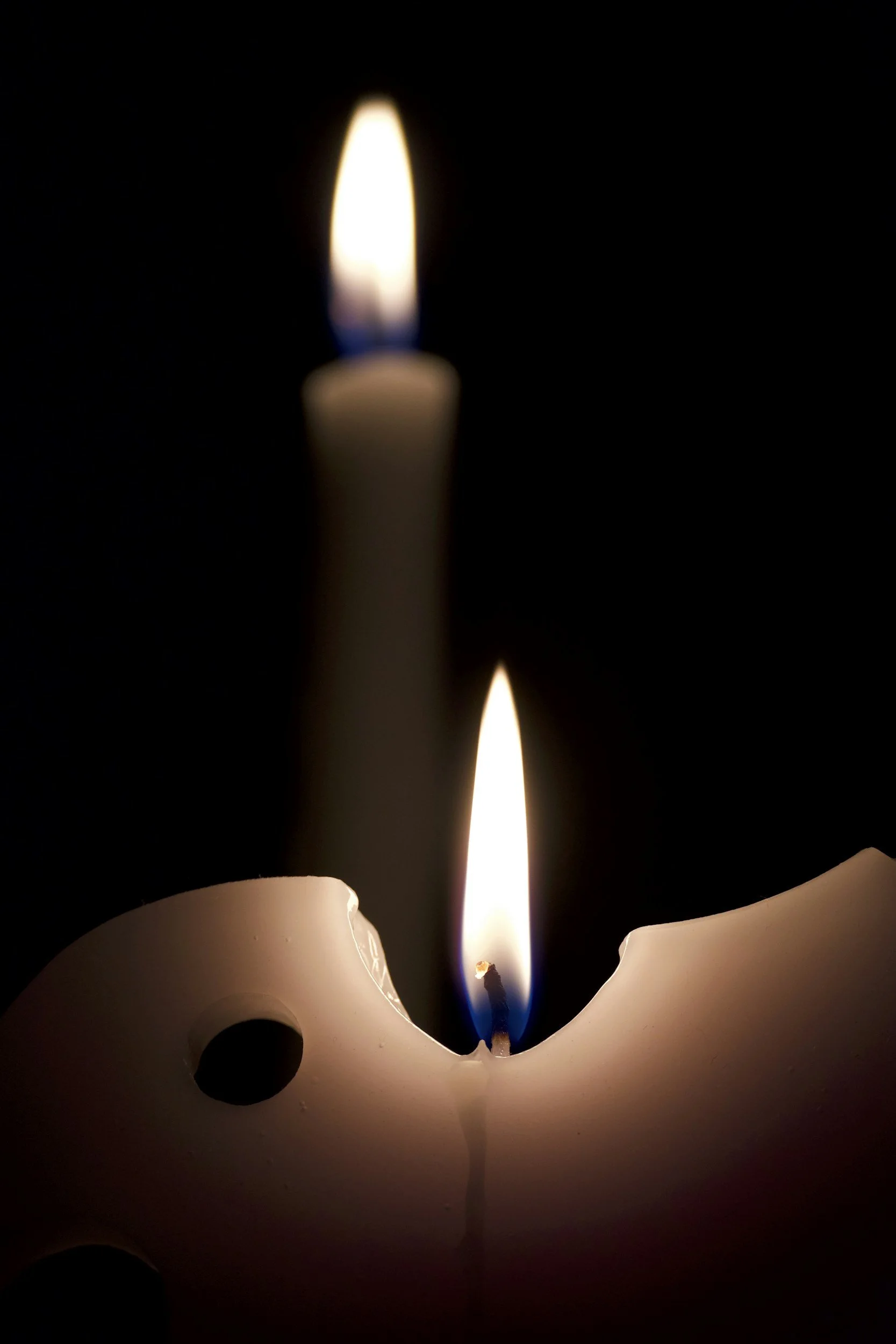 A candle with a flickering flame, melted wax, and a dark background.