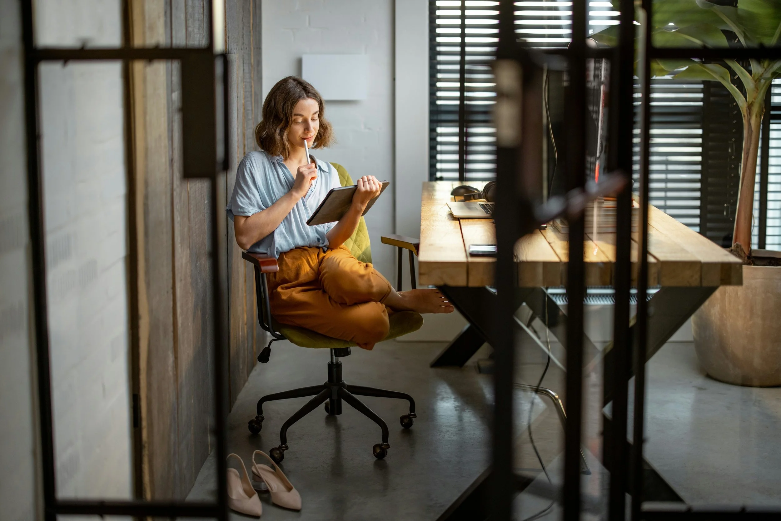 Woman sitting at a working desk holding a pen to her mouth while looking at a device symbolizing the convenience of online therapy intensives
