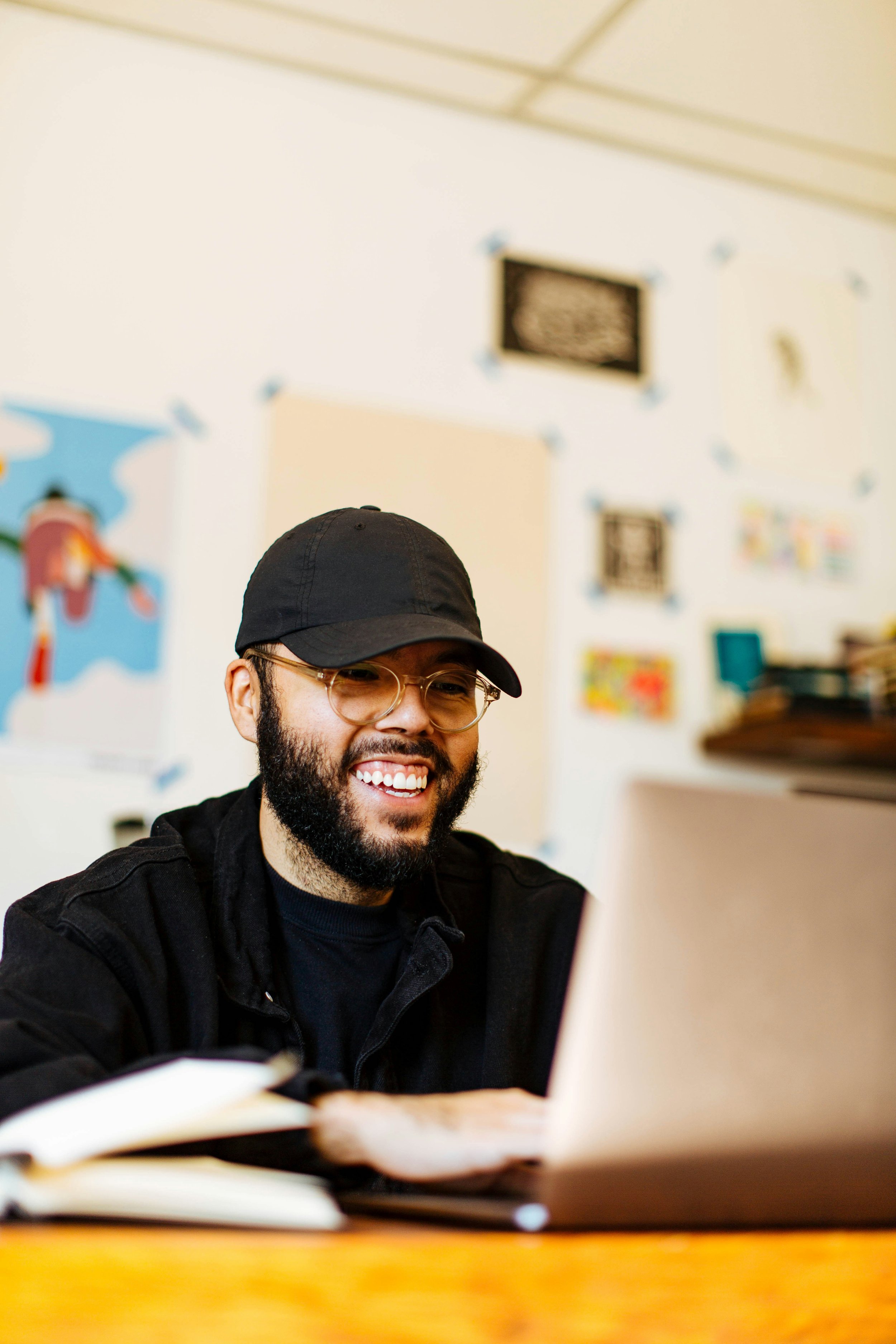 Online therapy in California and Texas - a picture of a man wearing a black shirt and hat in front of a laptop smiling to symbolize the ease and comfort of online therapy