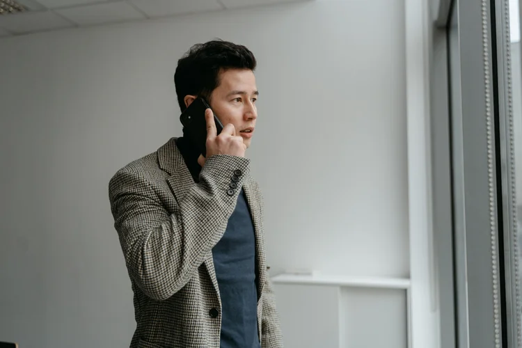 A finance professional in a checkered blazer on a phone call by an office window