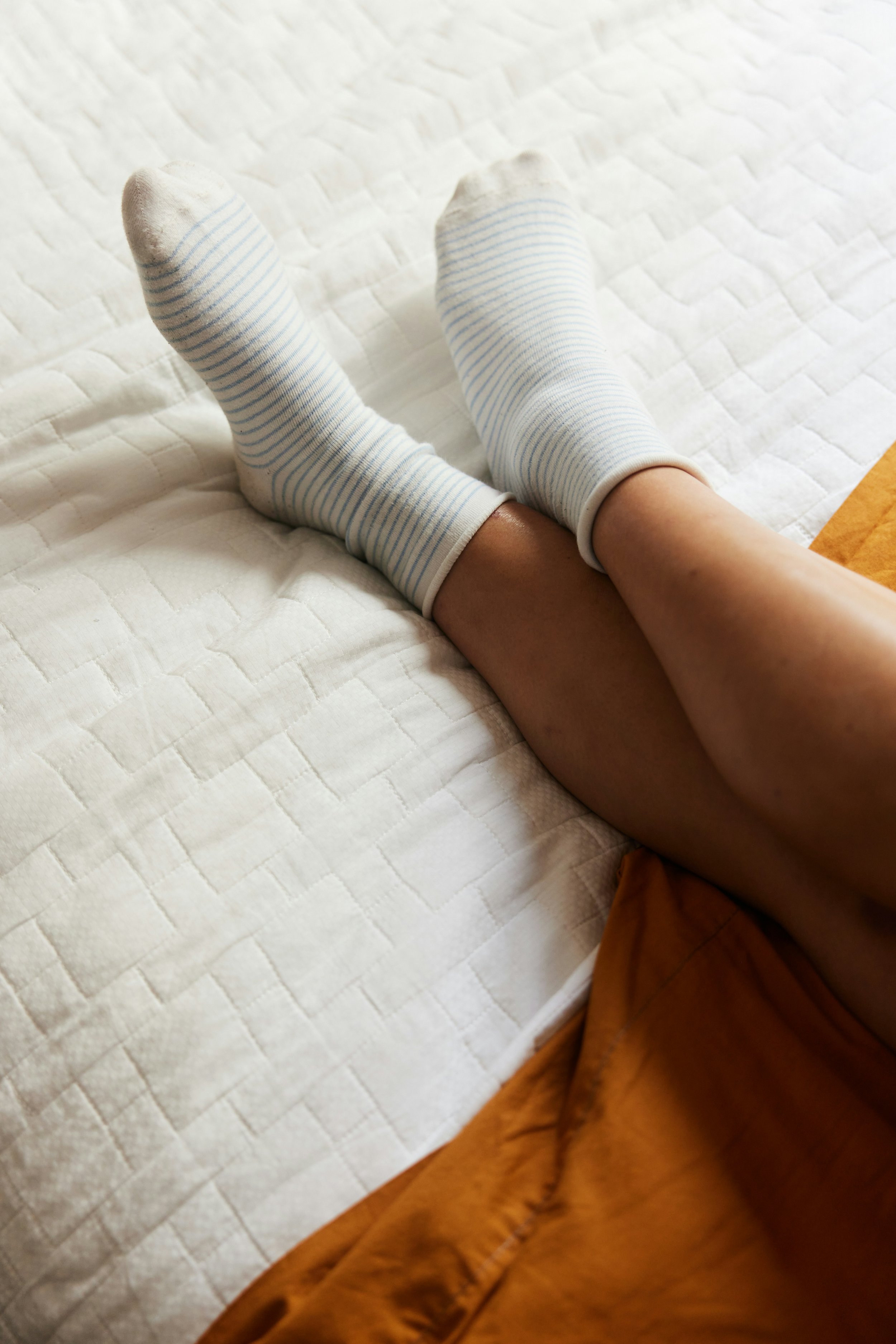 a picture of legs with white striped socks on the feet lying on a blanket symbolizing how experiencing burnout symptoms isn't always fixed by rest alone