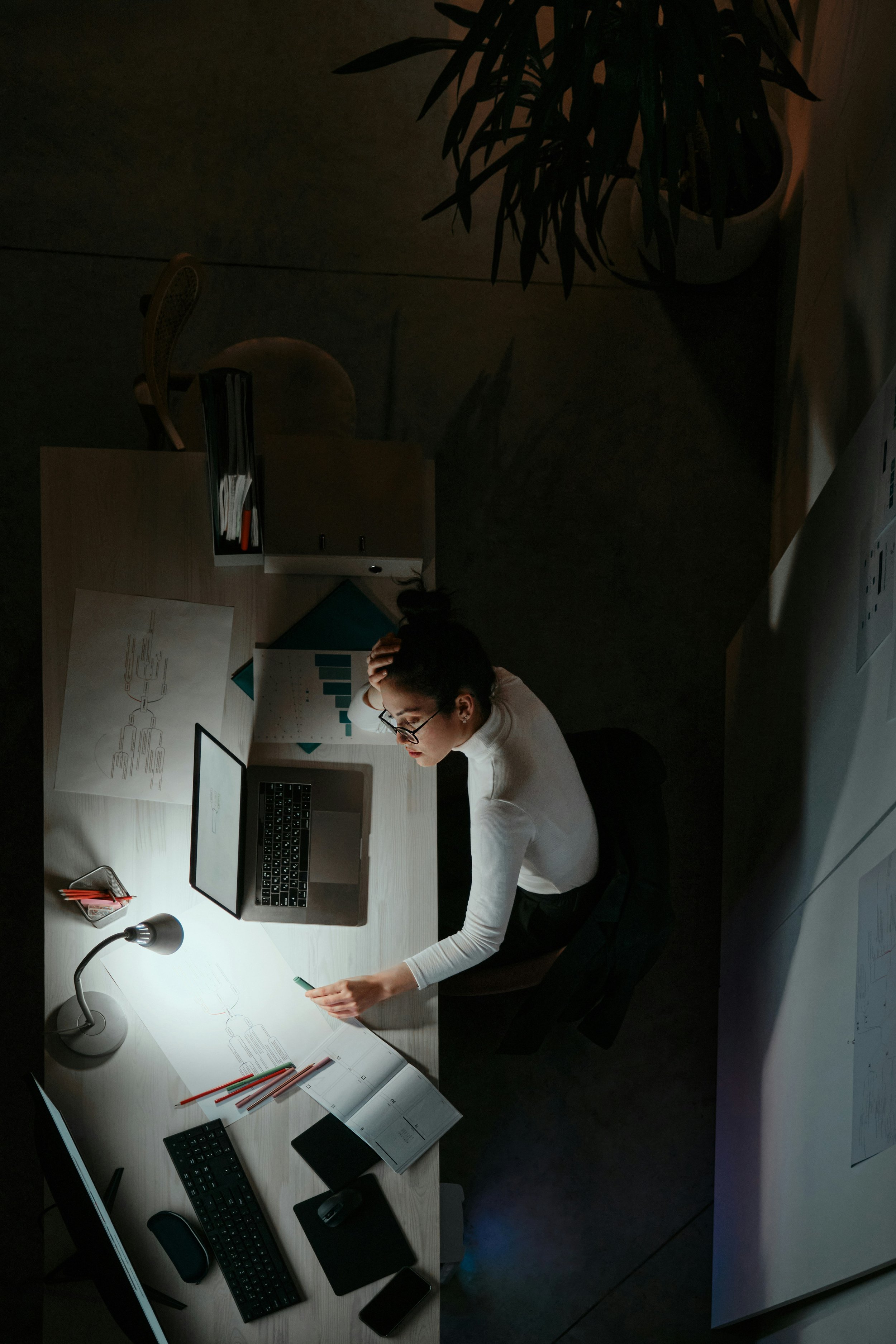 A woman with dark hair in a bun working at night at her desk and struggling with burnout
