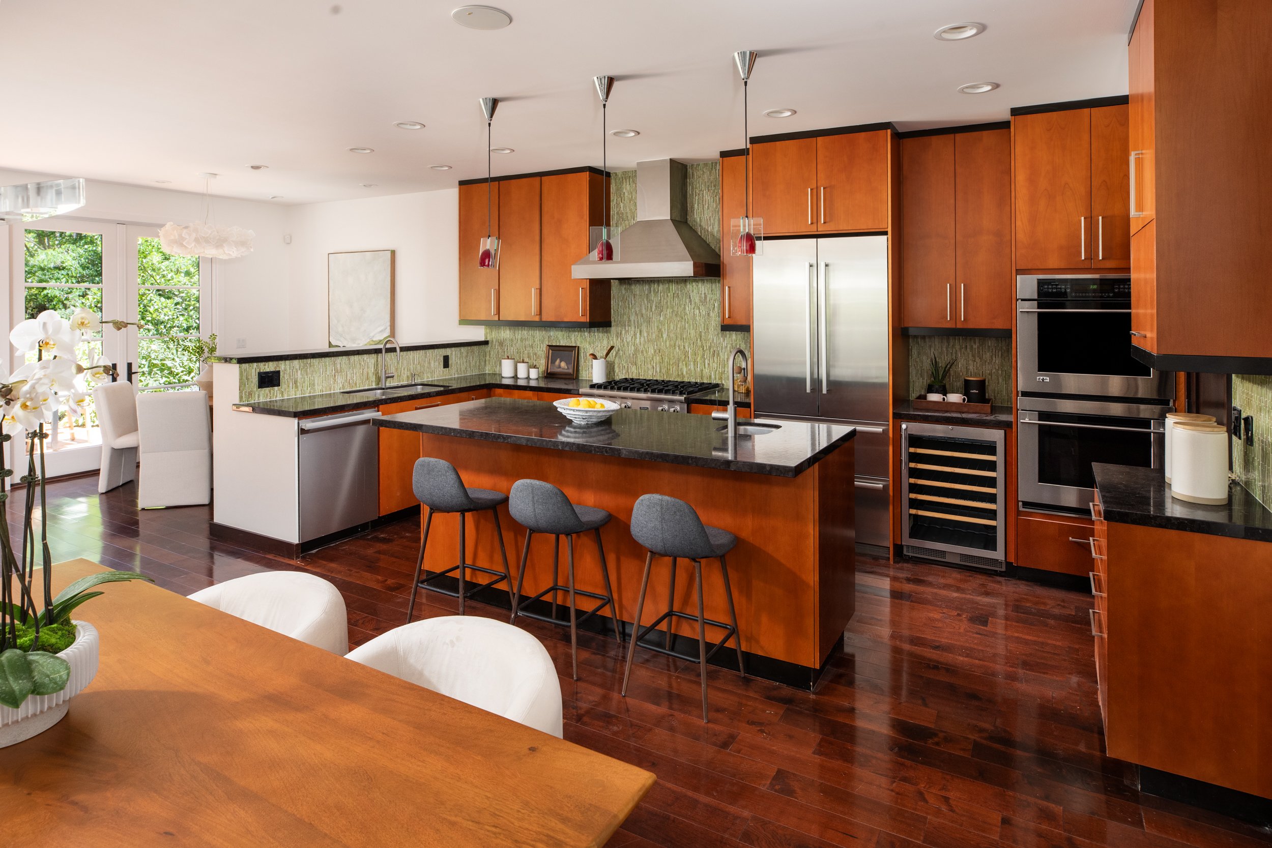 Modern kitchen with wooden cabinets, black countertops, stainless steel appliances, and pendant lights hanging above the island.